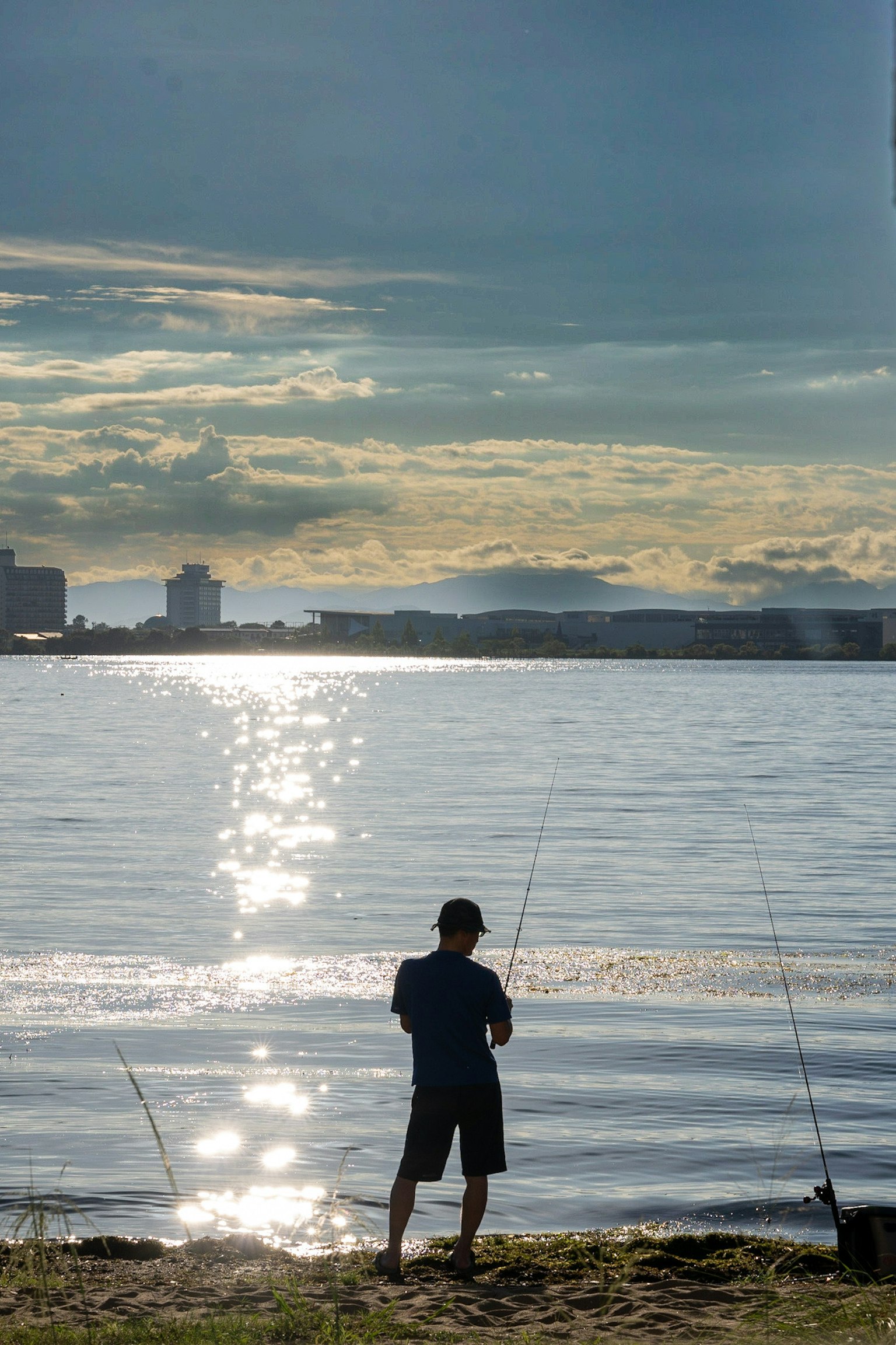 Silueta de un niño pescando junto al agua con reflejos del atardecer