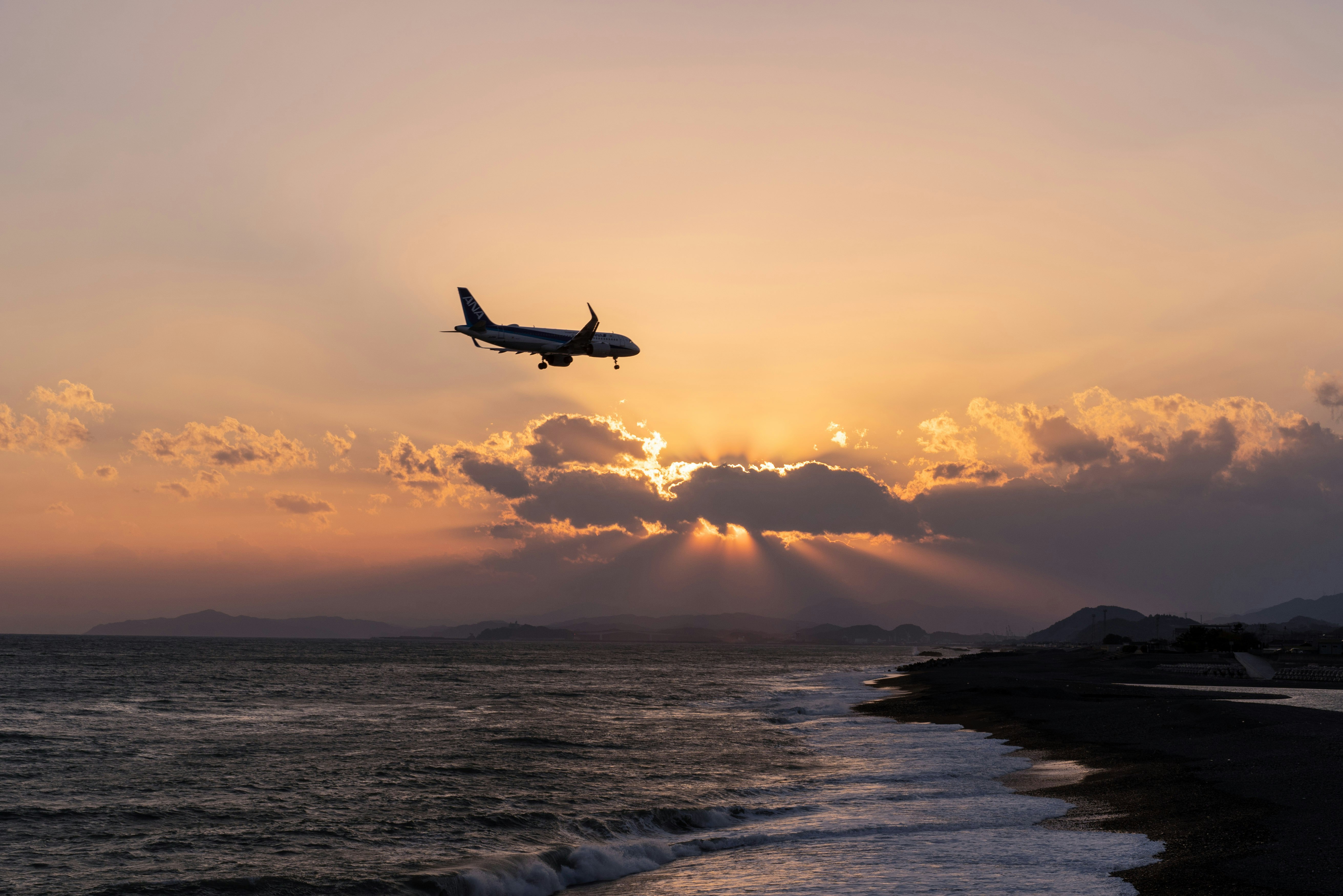 夕焼けの海岸を飛ぶ飛行機のシルエット