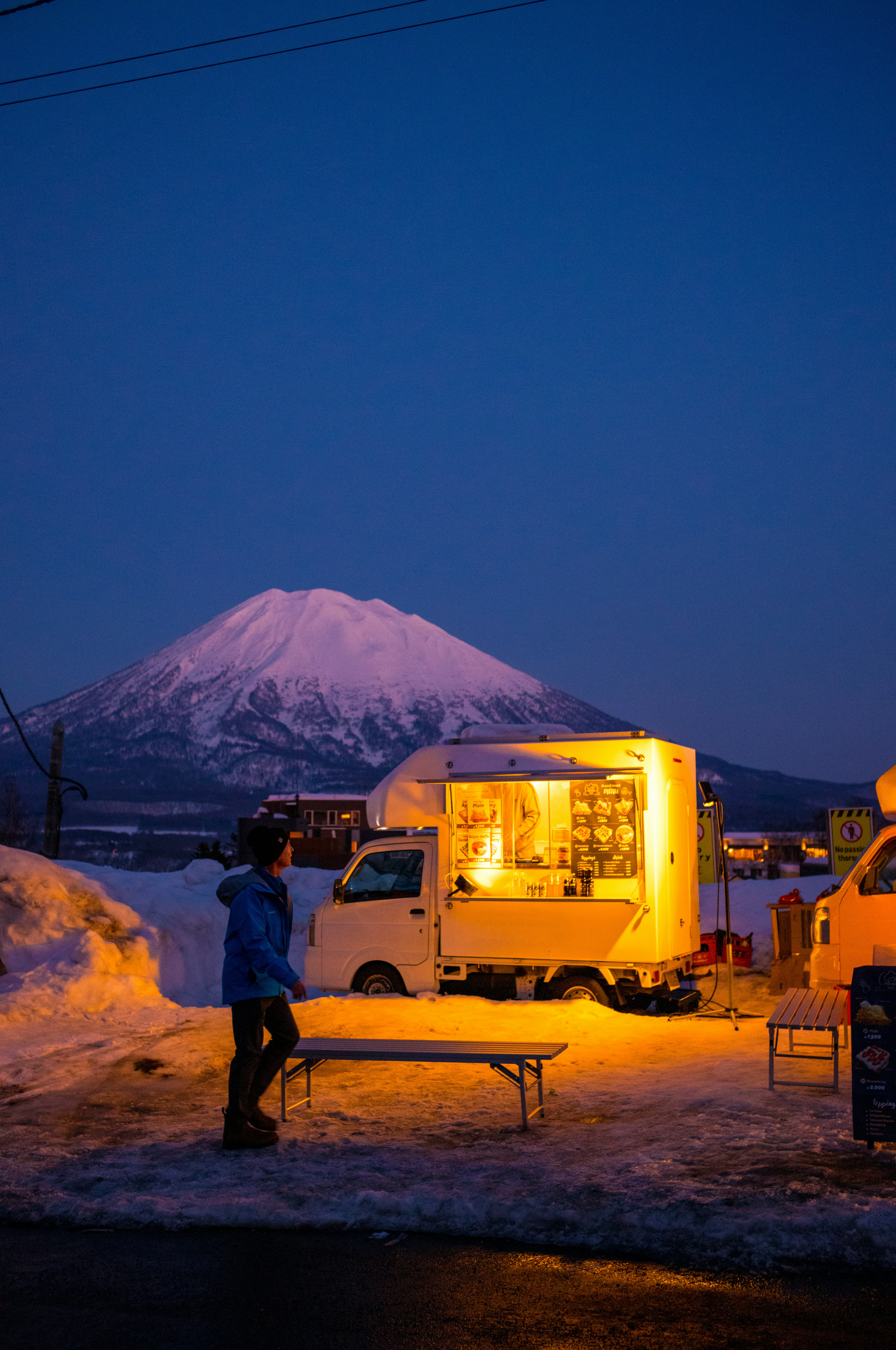 青い時間のニセコでトラックの屋台と雪の道、羊蹄山を望む