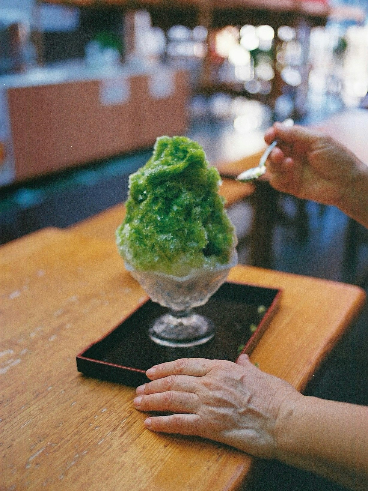 木のテーブルで手に乗せられた抹茶色のかき氷のようなスイーツ