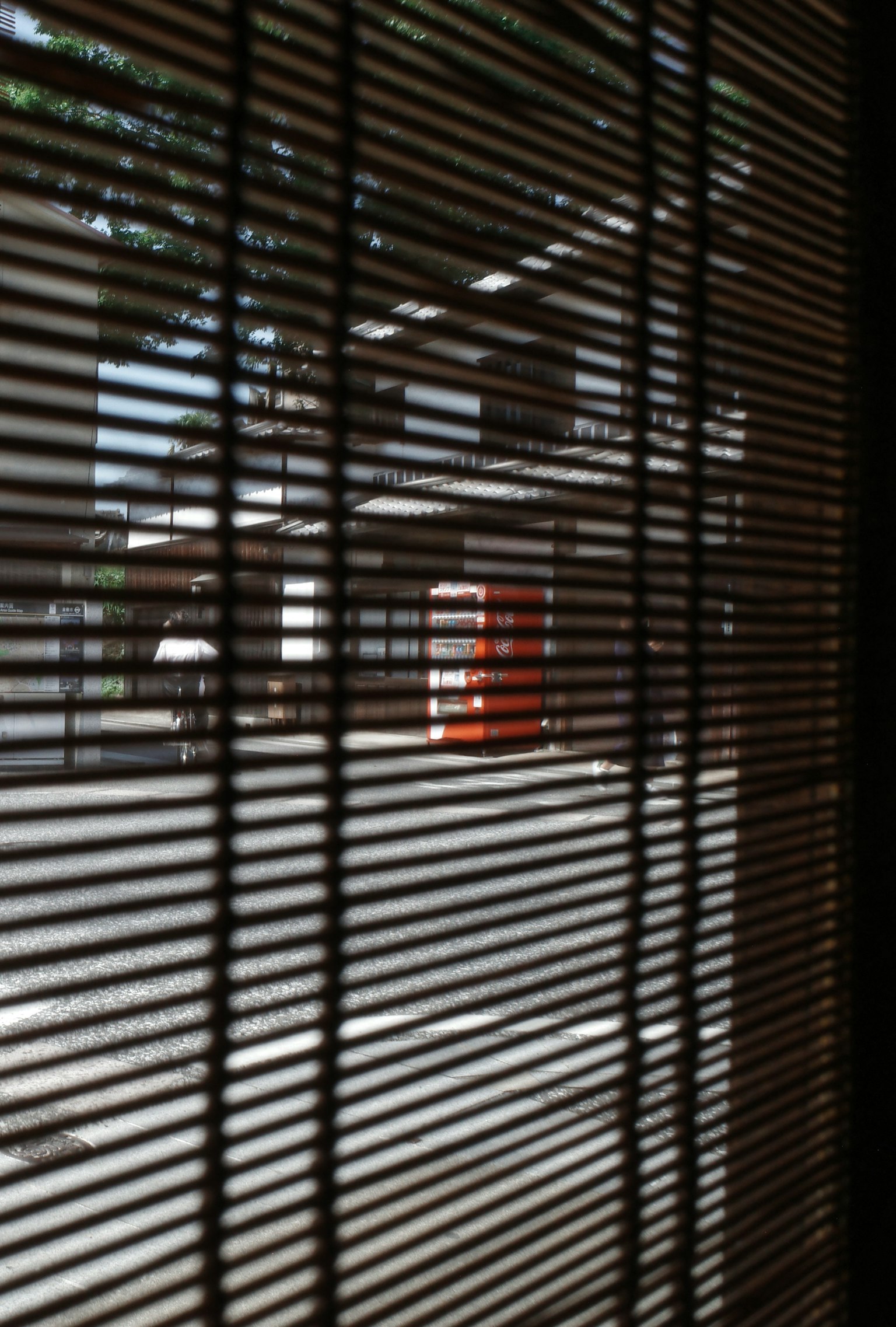 Blick auf eine Straße durch Jalousien mit einem orangefarbenen Briefkasten