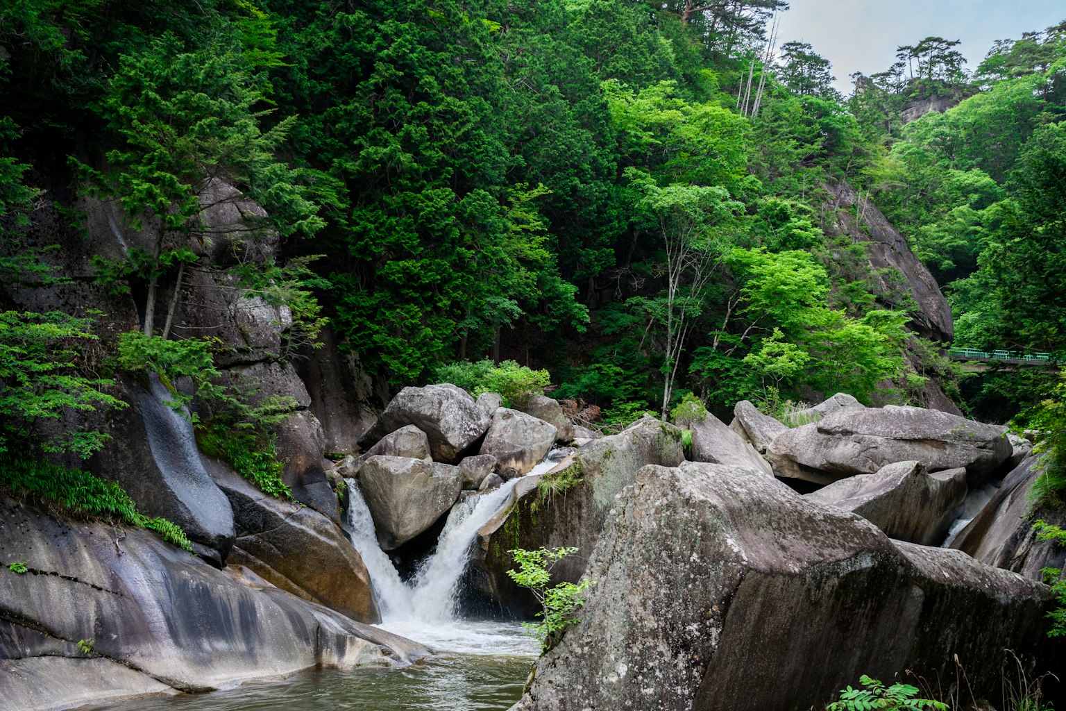 Hutan hijau subur dengan air terjun batu besar membingkai aliran air