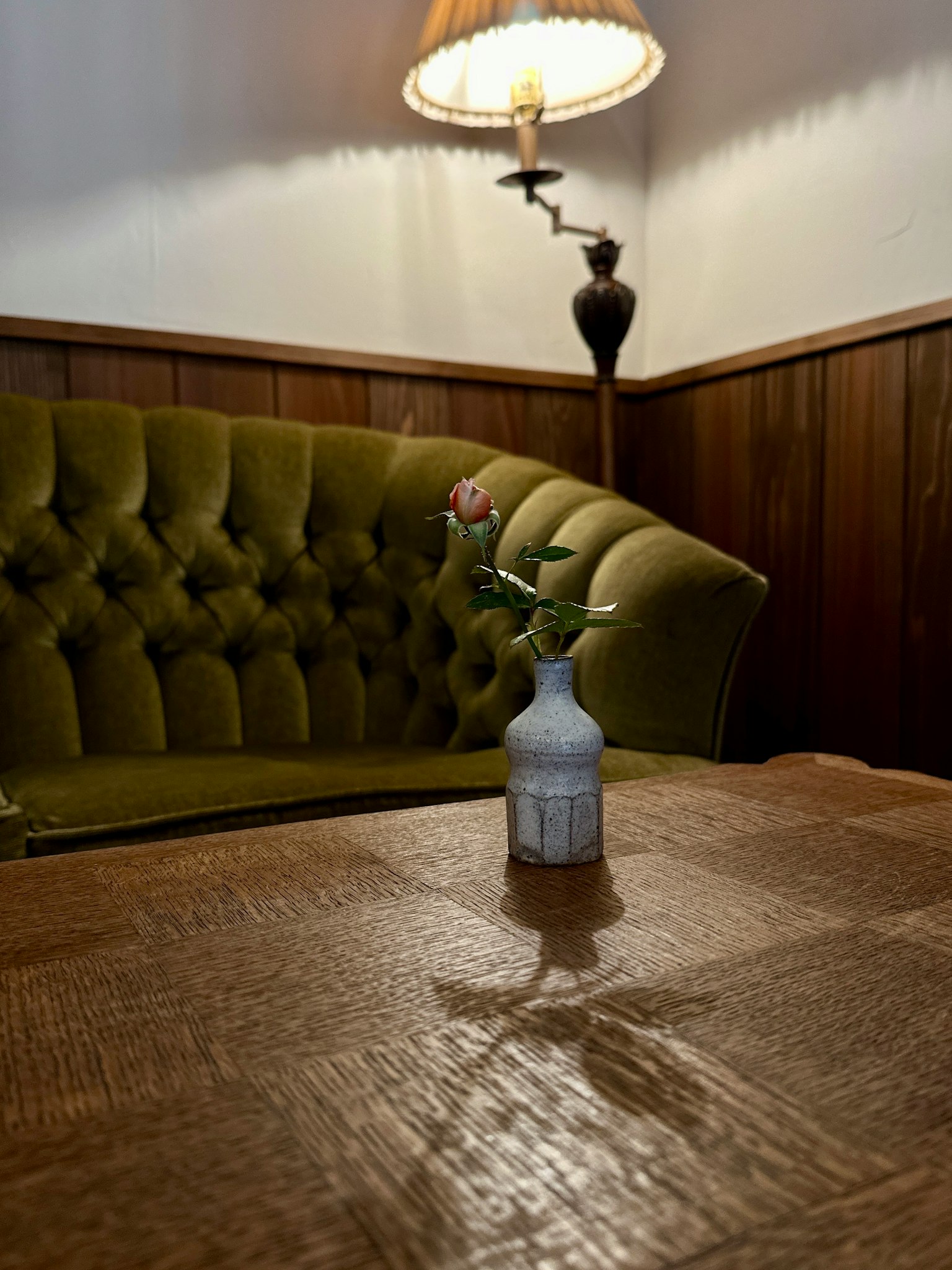 ฉากในบ้านที่มีโซฟาสีเขียวและแจกันเล็กๆ บนโต๊ะไม้