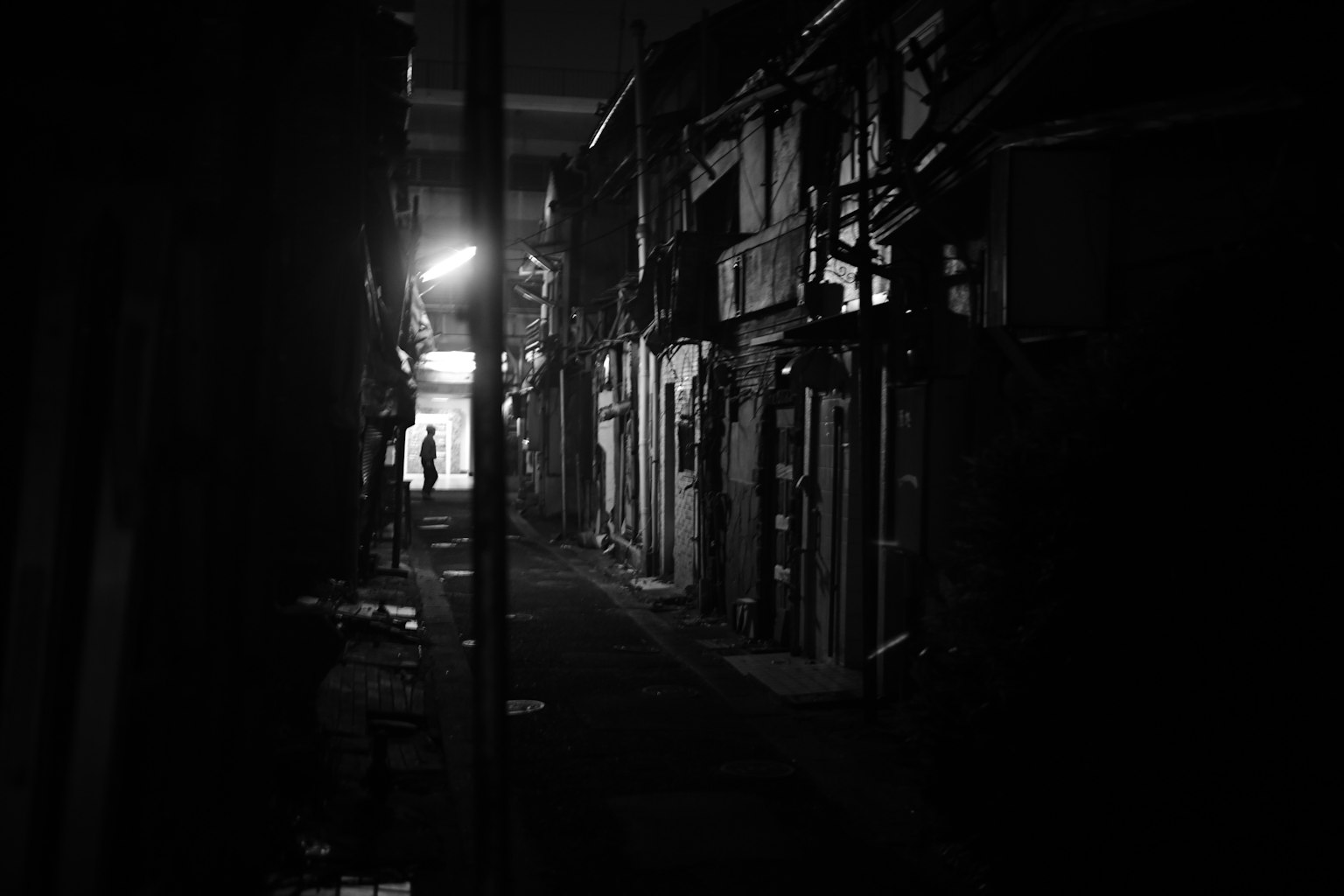 Black and white photo of a narrow alley with buildings and streetlight