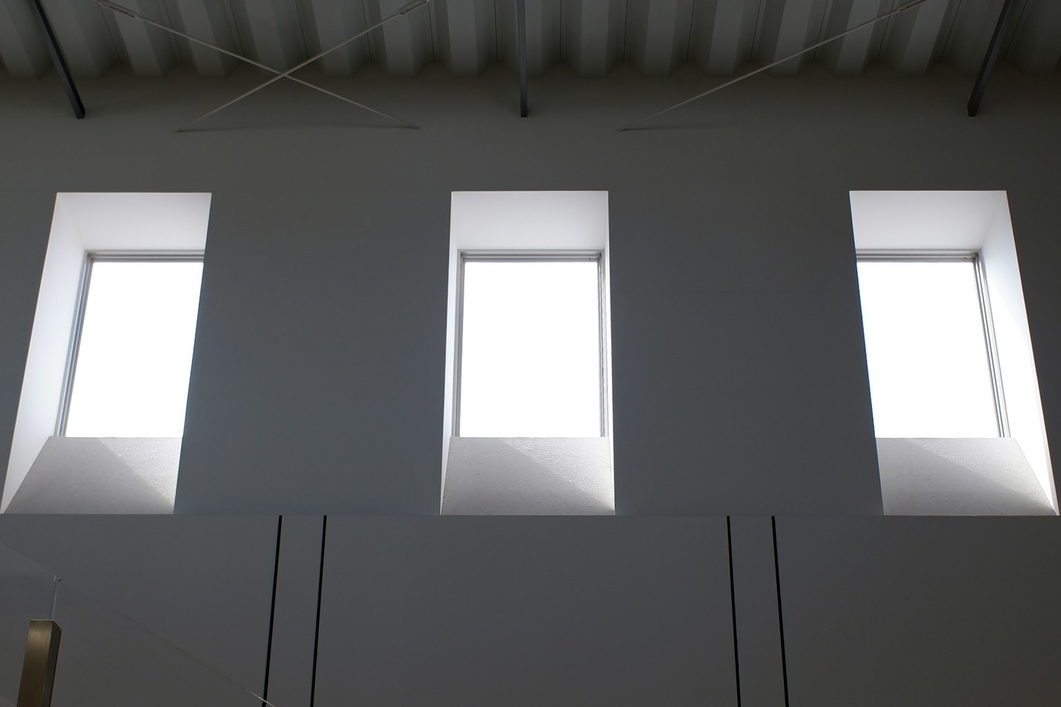 Drei rechteckige Fenster an einer weißen Wand in einem minimalistischen Innenraum