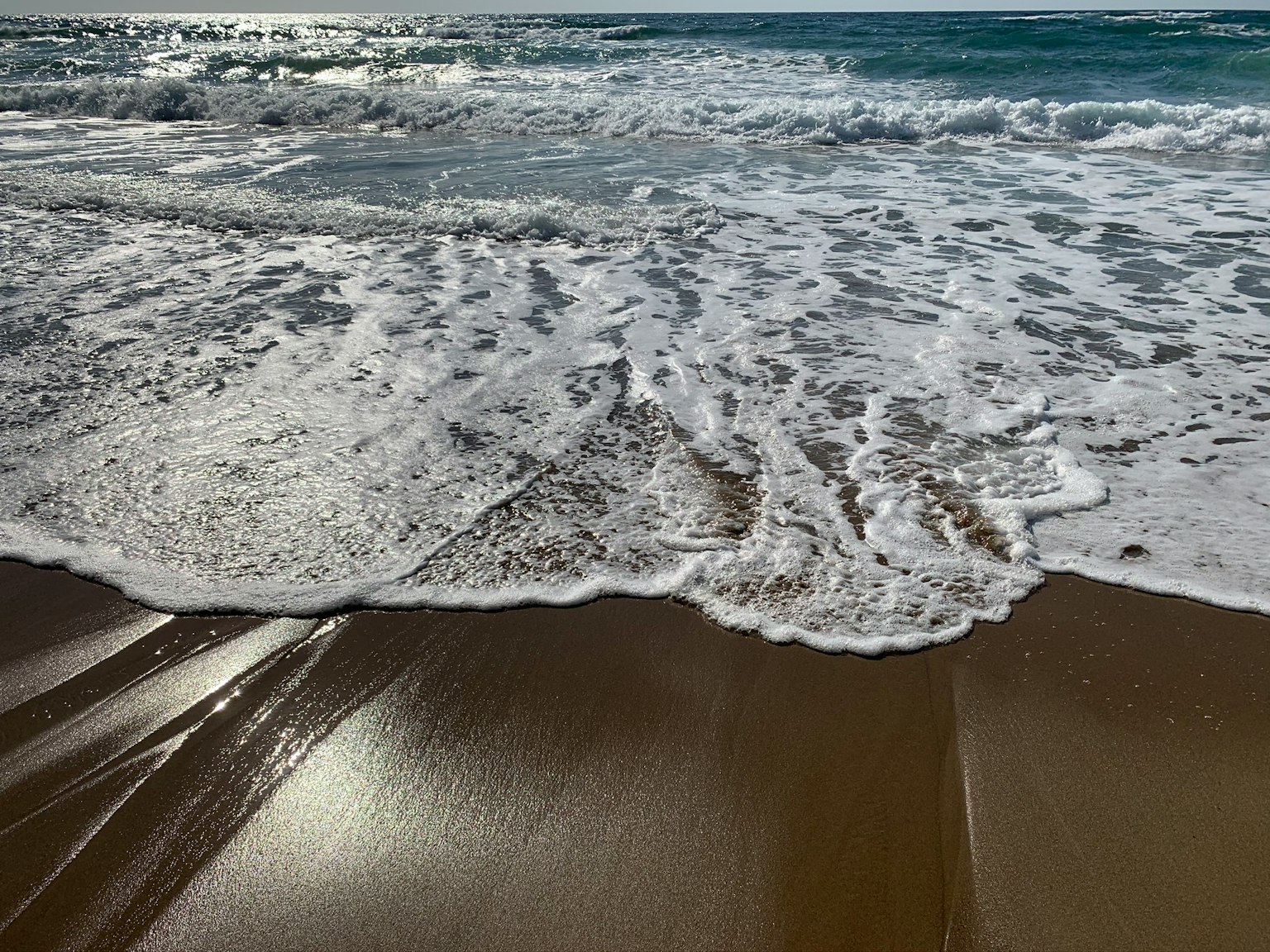 Olas rompiendo en una playa de arena con agua brillante