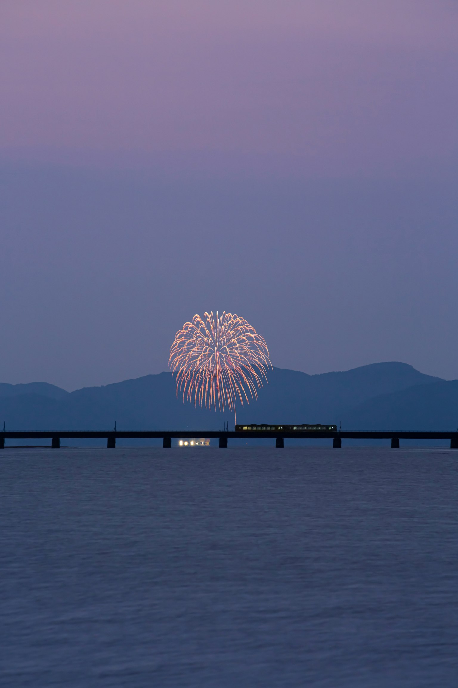 Fuochi d'artificio sull'acqua con un ponte al crepuscolo