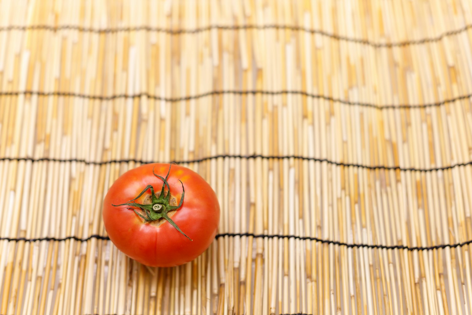 Une tomate rouge placée sur un tapis en bambou