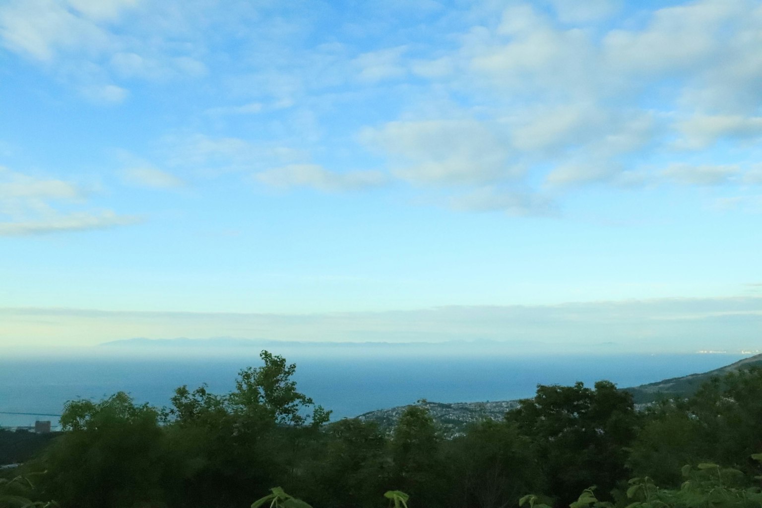 Pemandangan langit biru dan laut dengan pepohonan hijau di latar depan