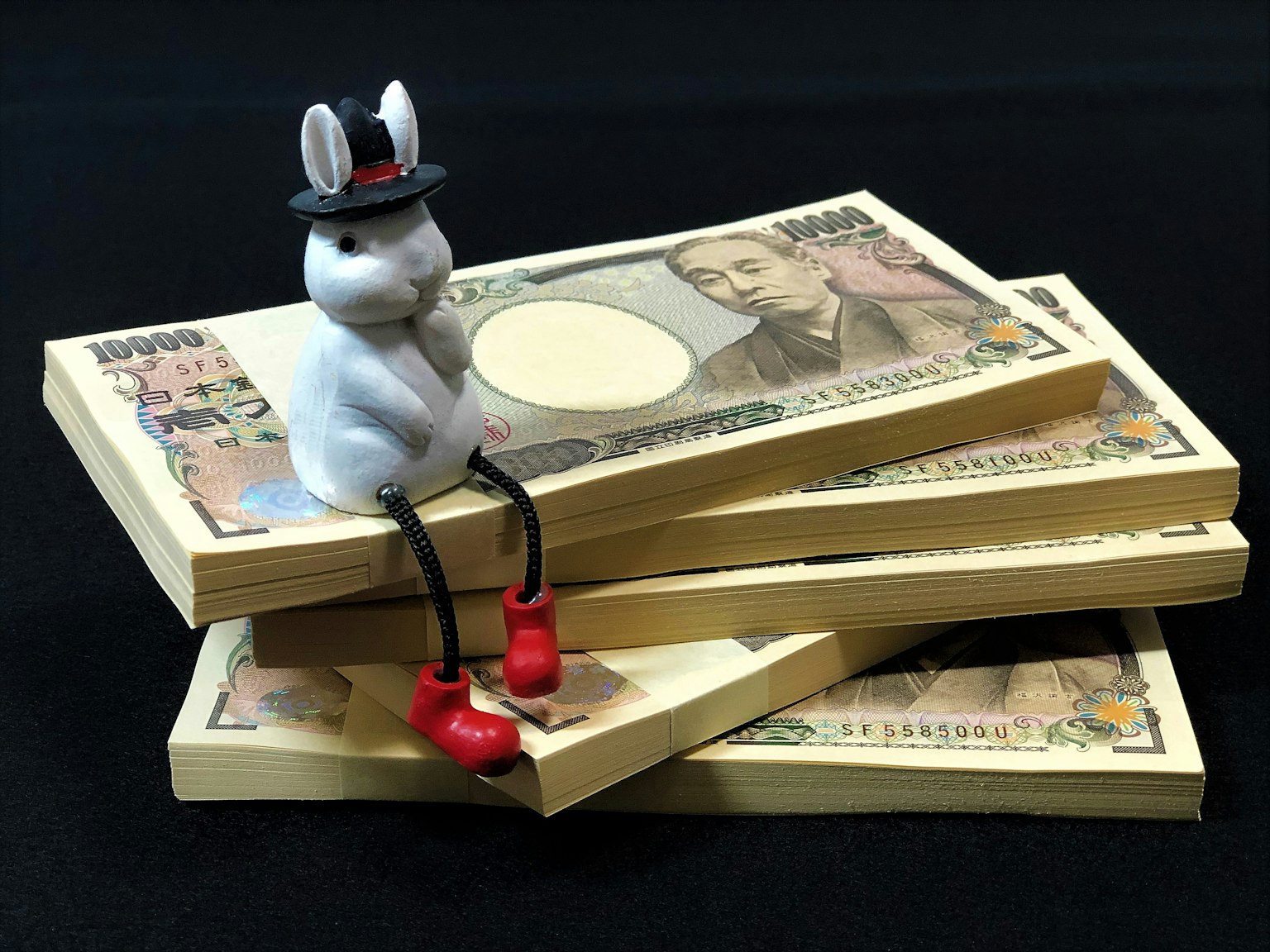 A rabbit figurine wearing a hat sitting on a stack of money