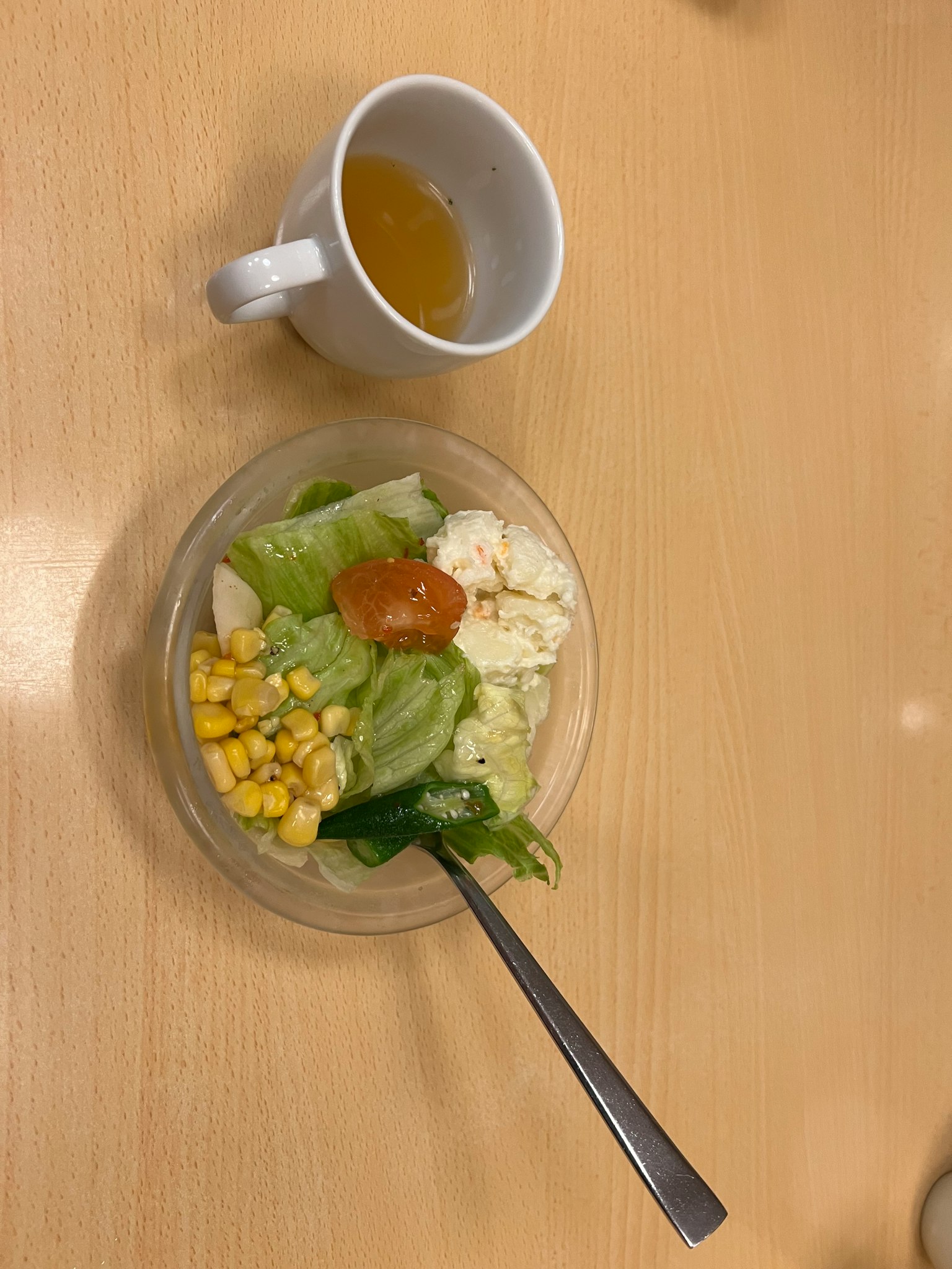 Un tazón de ensalada con lechuga, maíz y tomate al lado de una taza de té