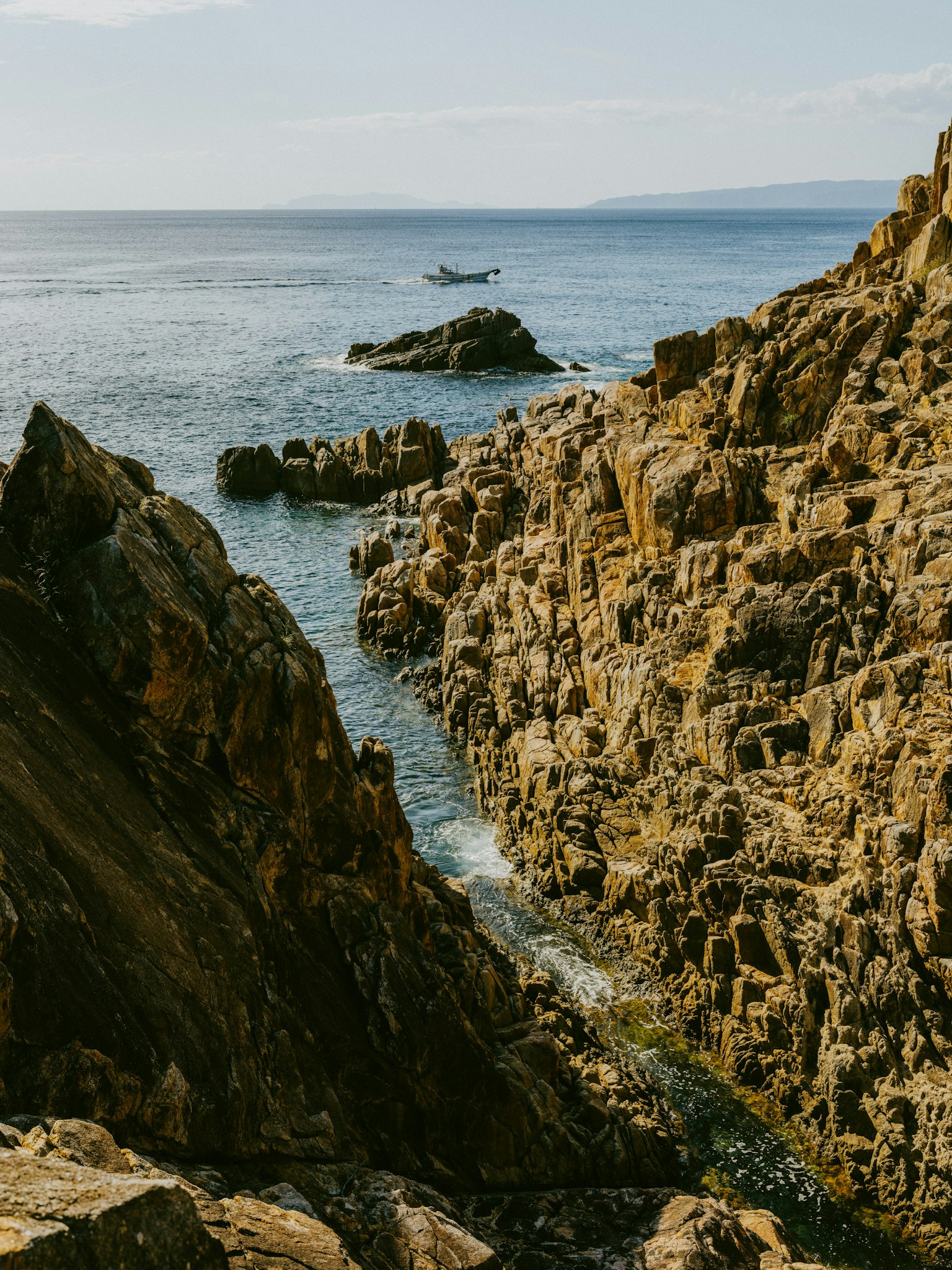 Vue pittoresque d'une côte rocheuse avec des vagues océaniques et un petit bateau au loin