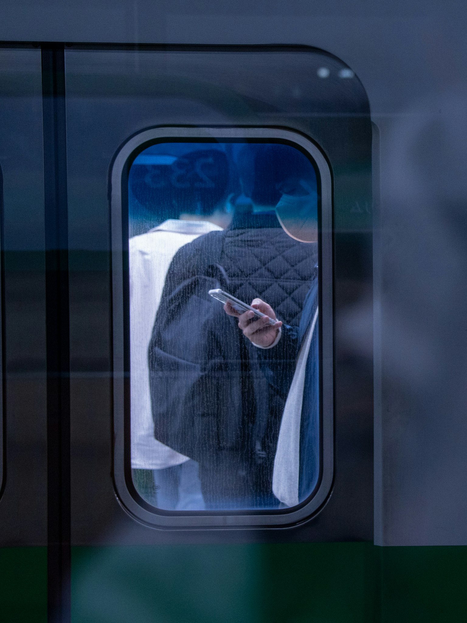 電車の窓から見える人々の後ろ姿とスマートフォンを持つ手