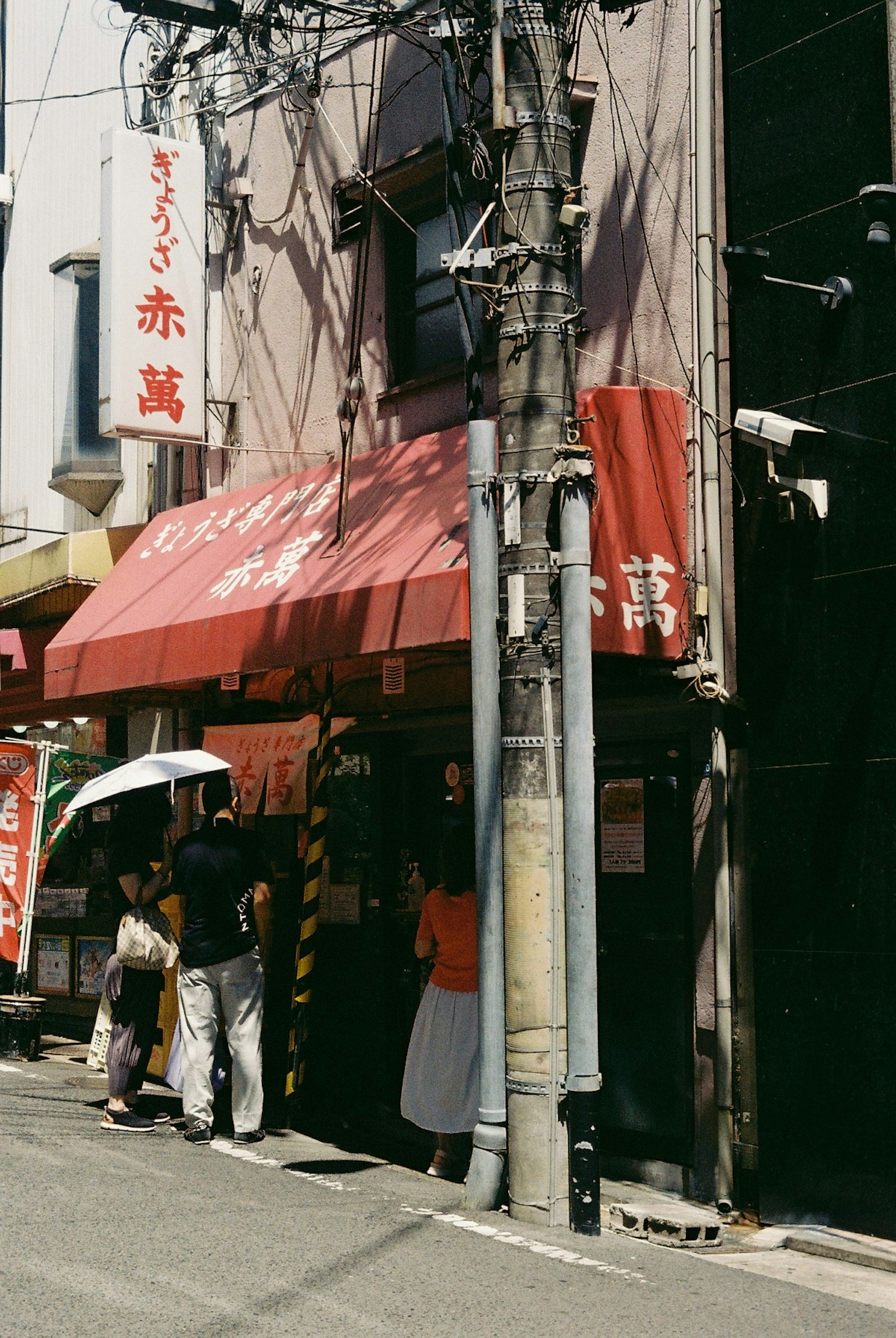 ภายนอกของร้านอาหารที่มีมุงสีแดงและผู้คนด้านนอก