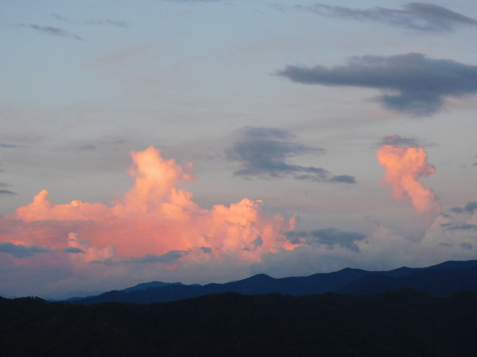 Nubes rosas contra un cielo azul con siluetas de montañas
