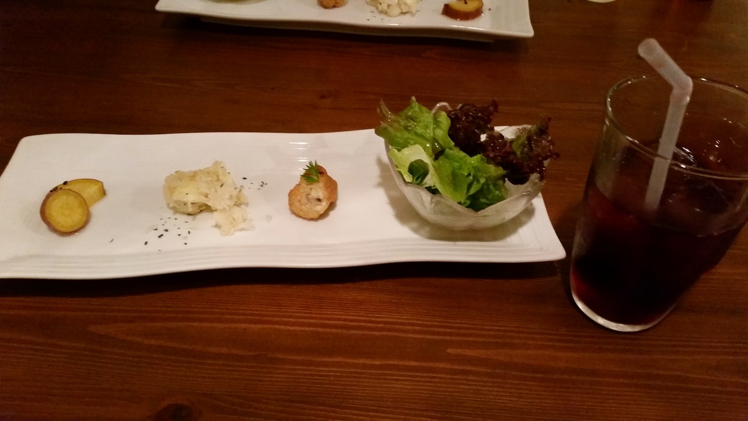 Plate with assorted appetizers and salad alongside a drink