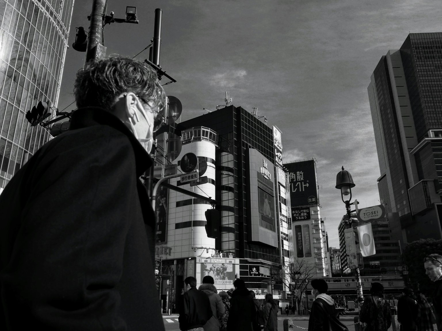 Man wearing a mask gazing at a busy intersection in black and white