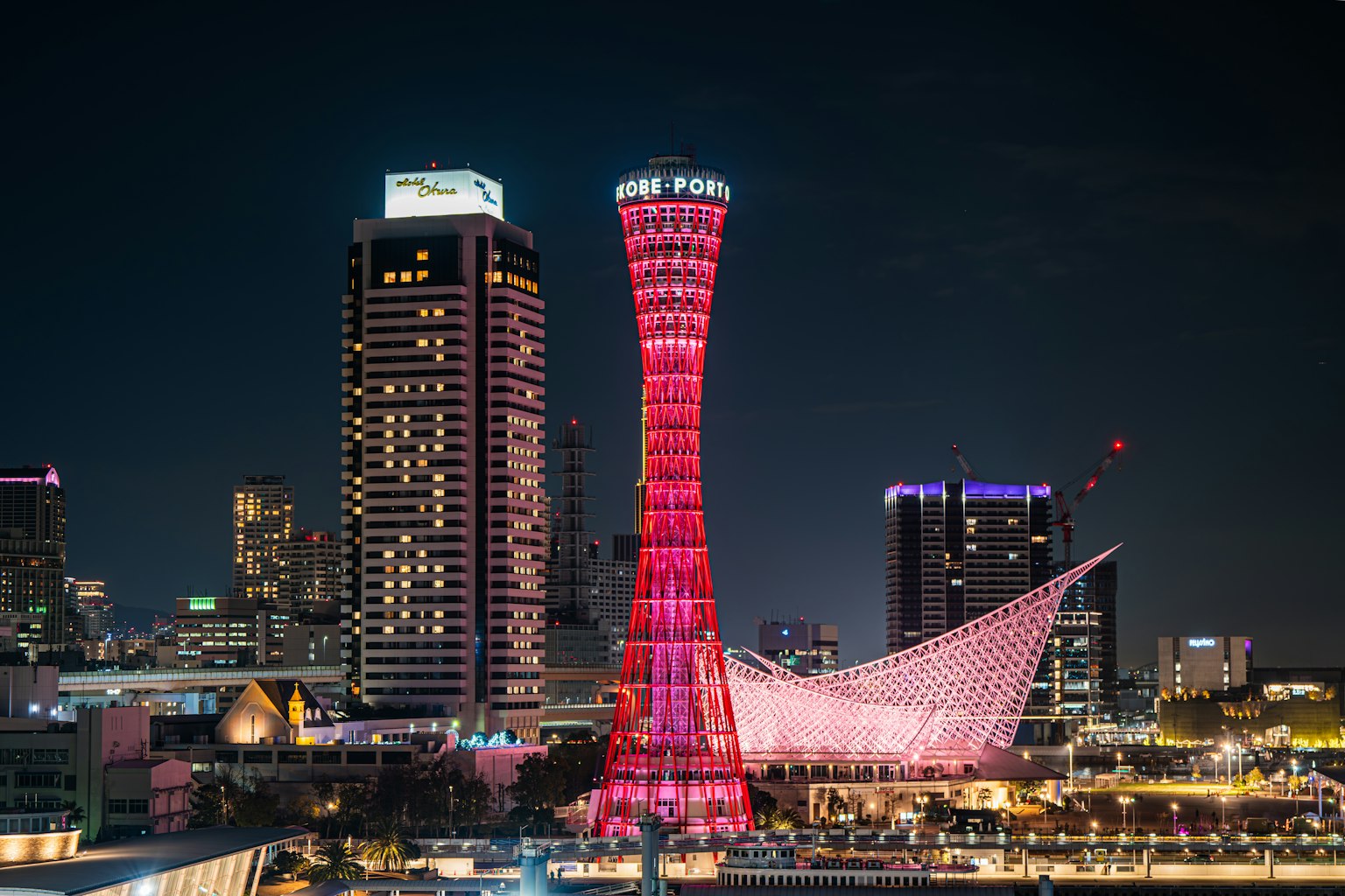 Menara Pelabuhan Kobe di malam hari diterangi dengan warna merah muda cerah dikelilingi gedung pencakar langit