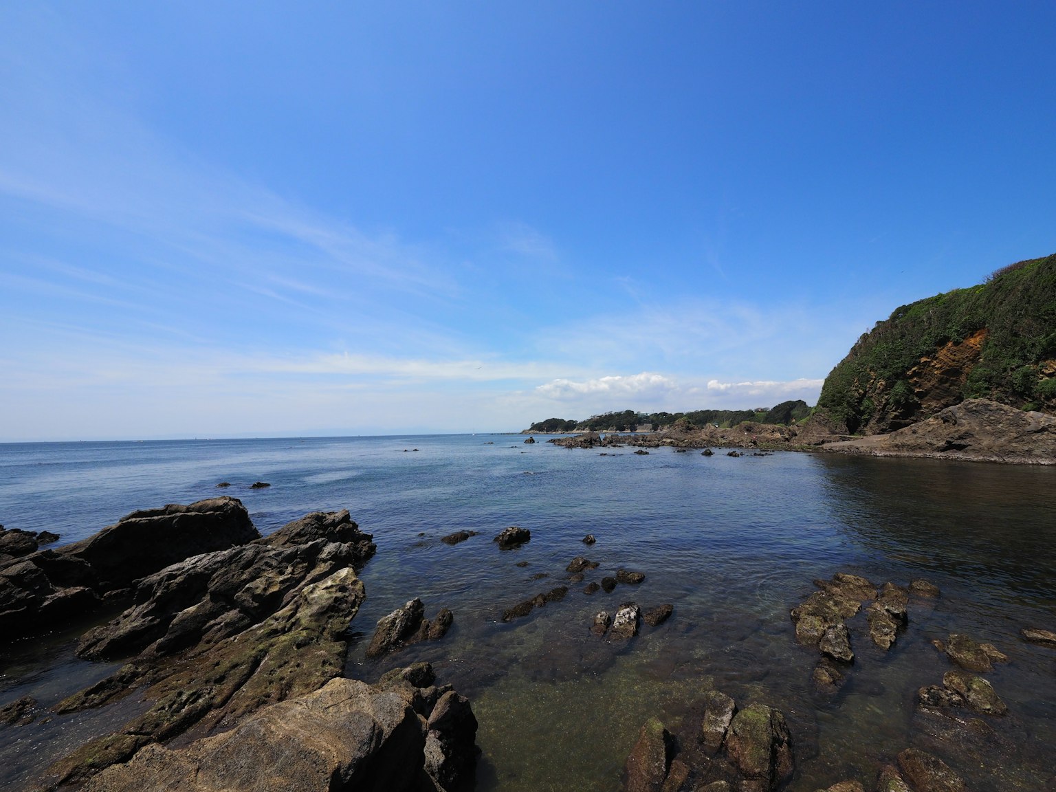Malersiche Aussicht auf ein ruhiges Meer und blauen Himmel mit felsiger Küste und grünem Hügel