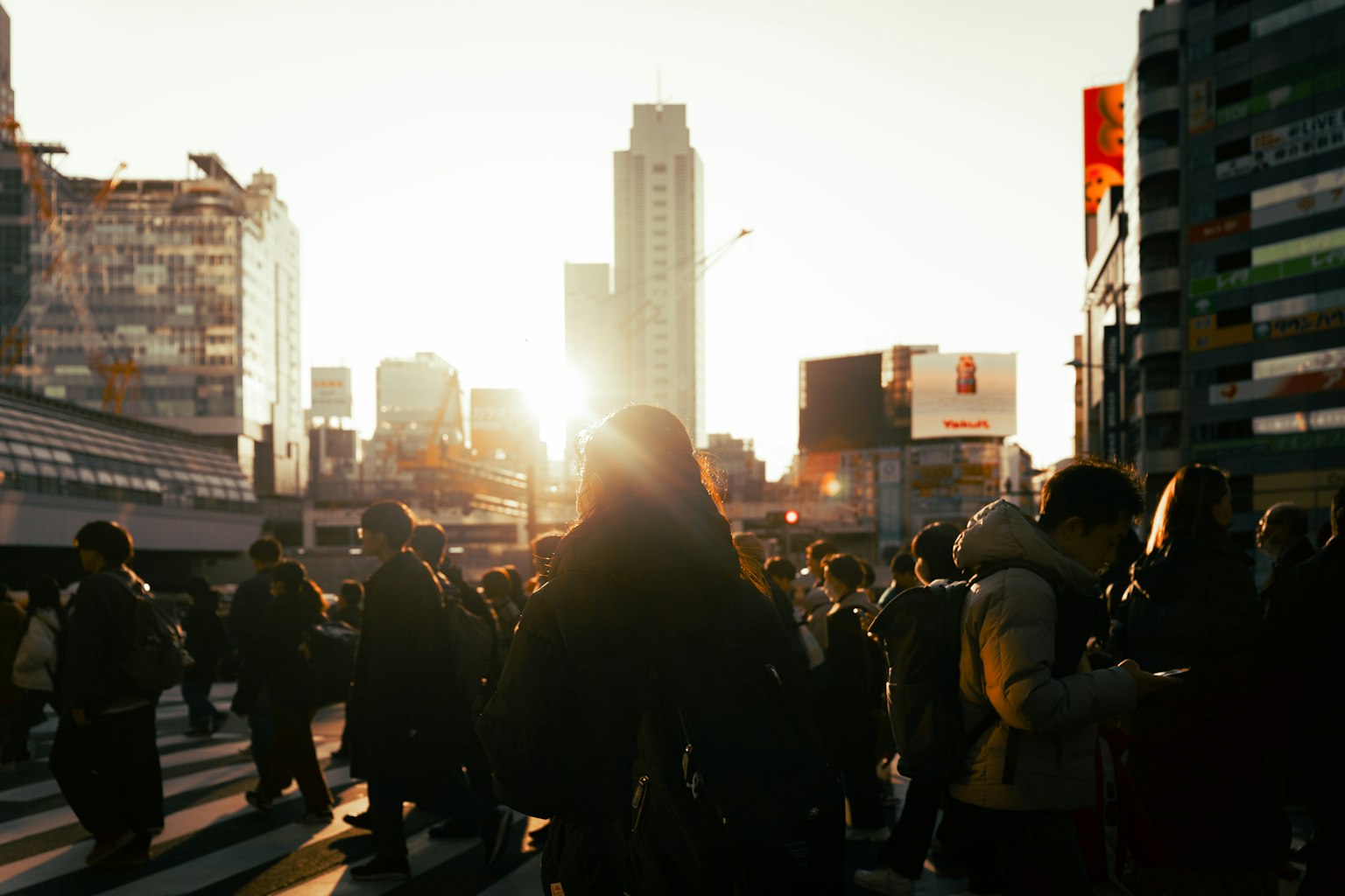 Foule de personnes traversant un carrefour urbain avec le coucher de soleil en arrière-plan