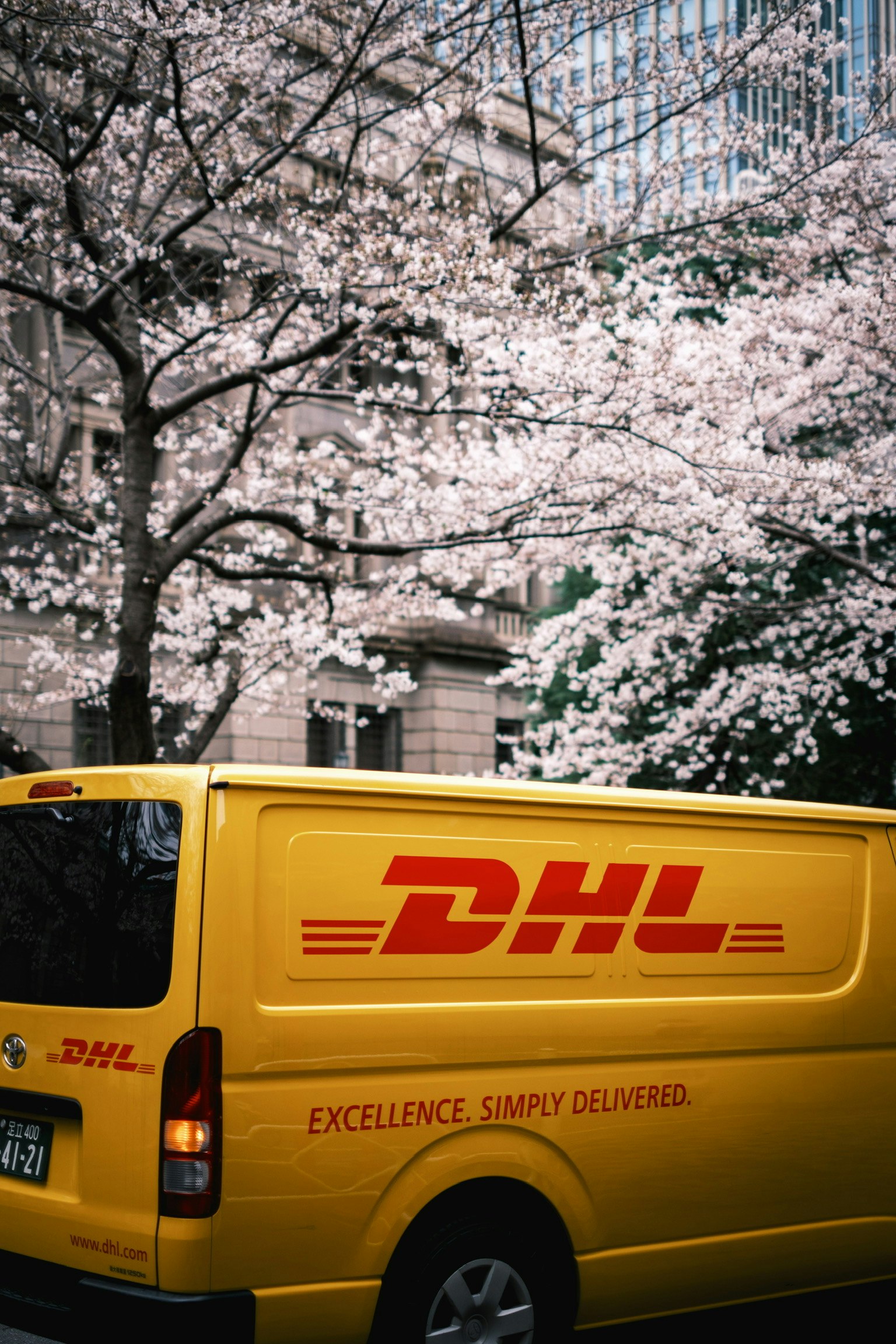 gelber DHL-Lieferwagen an einer Straßenecke unter Kirschblüten