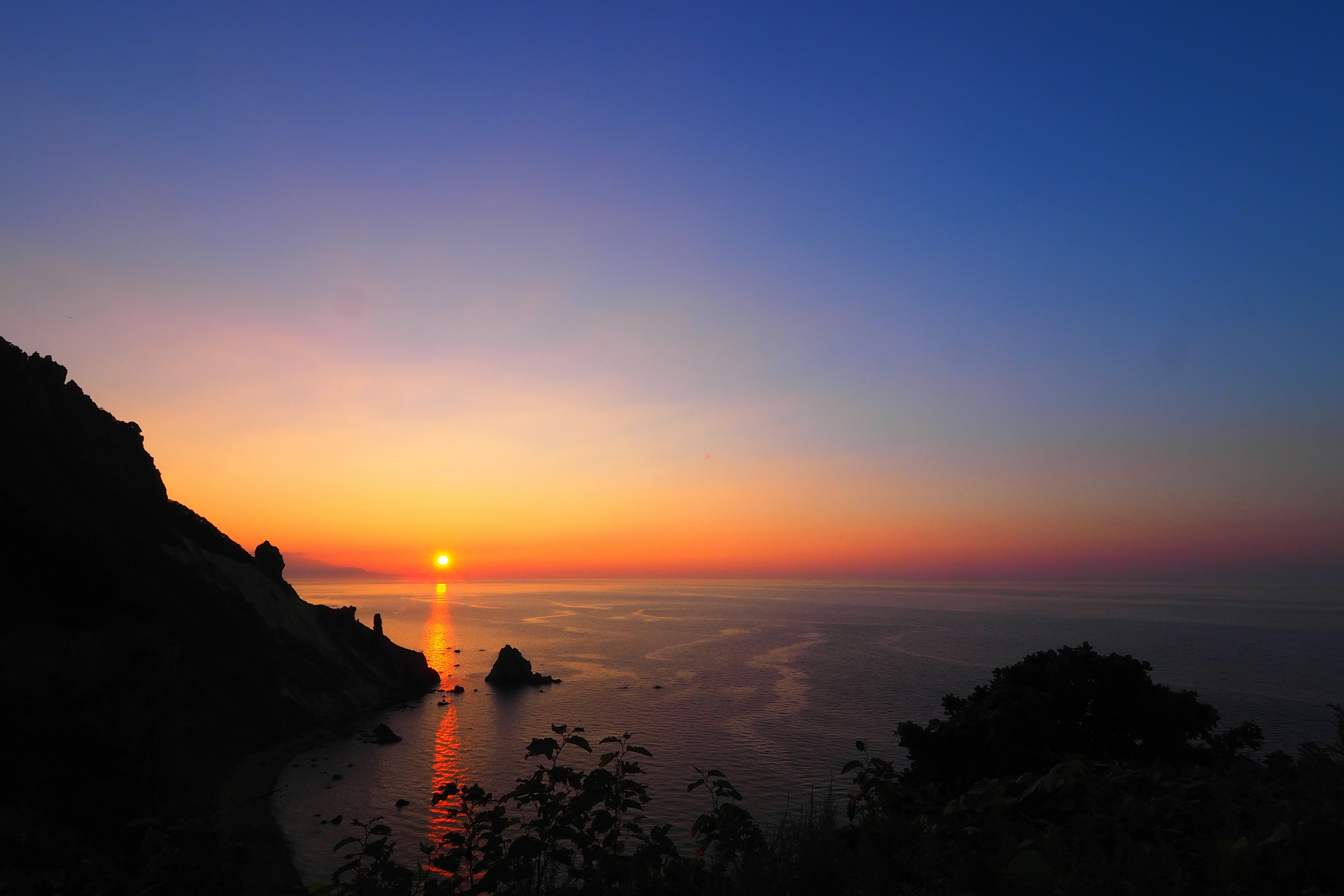 夕焼けの海と岩場のシルエットが広がる海岸の風景