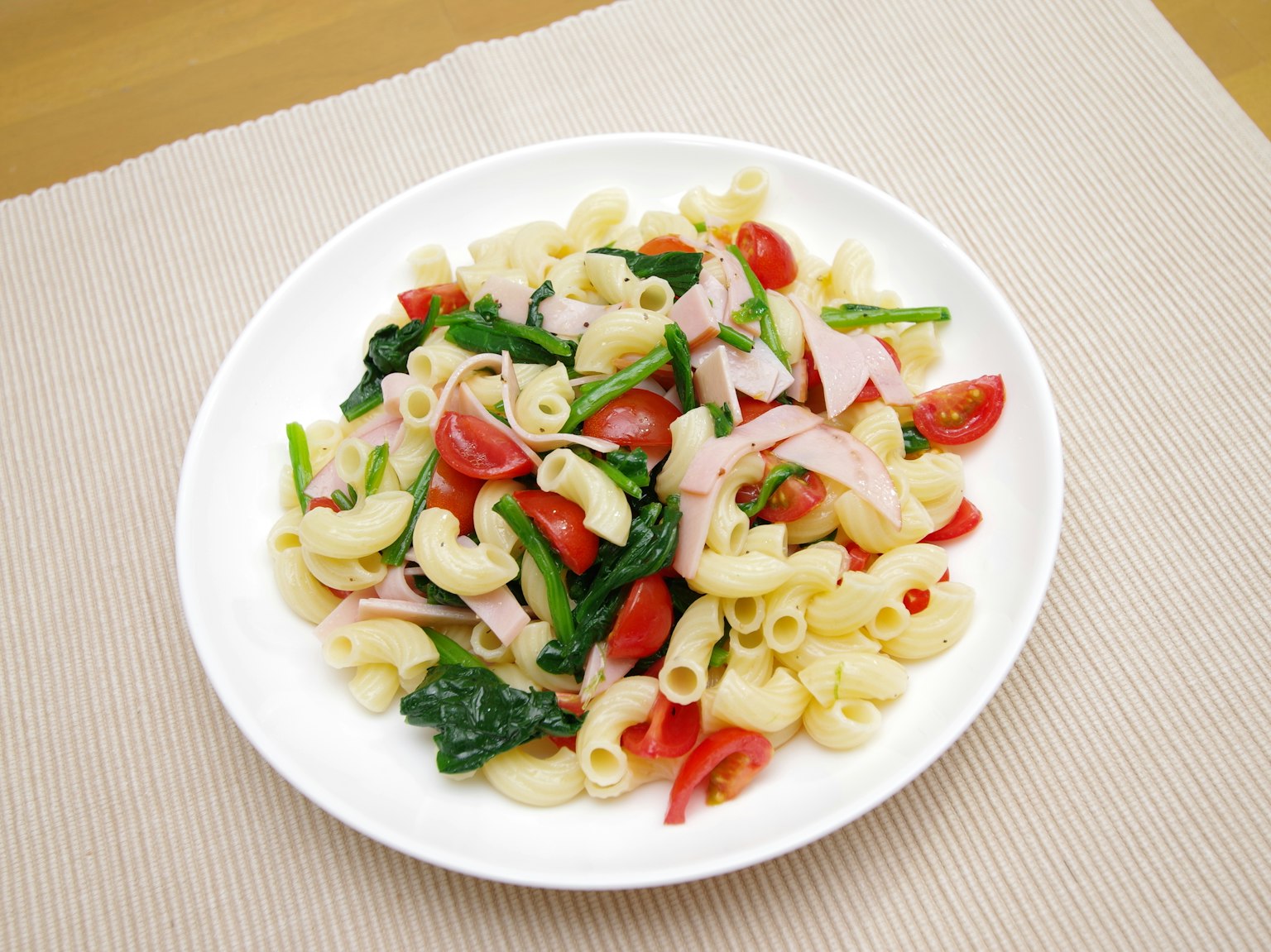 Plate of pasta salad with elbow macaroni tomatoes ham spinach