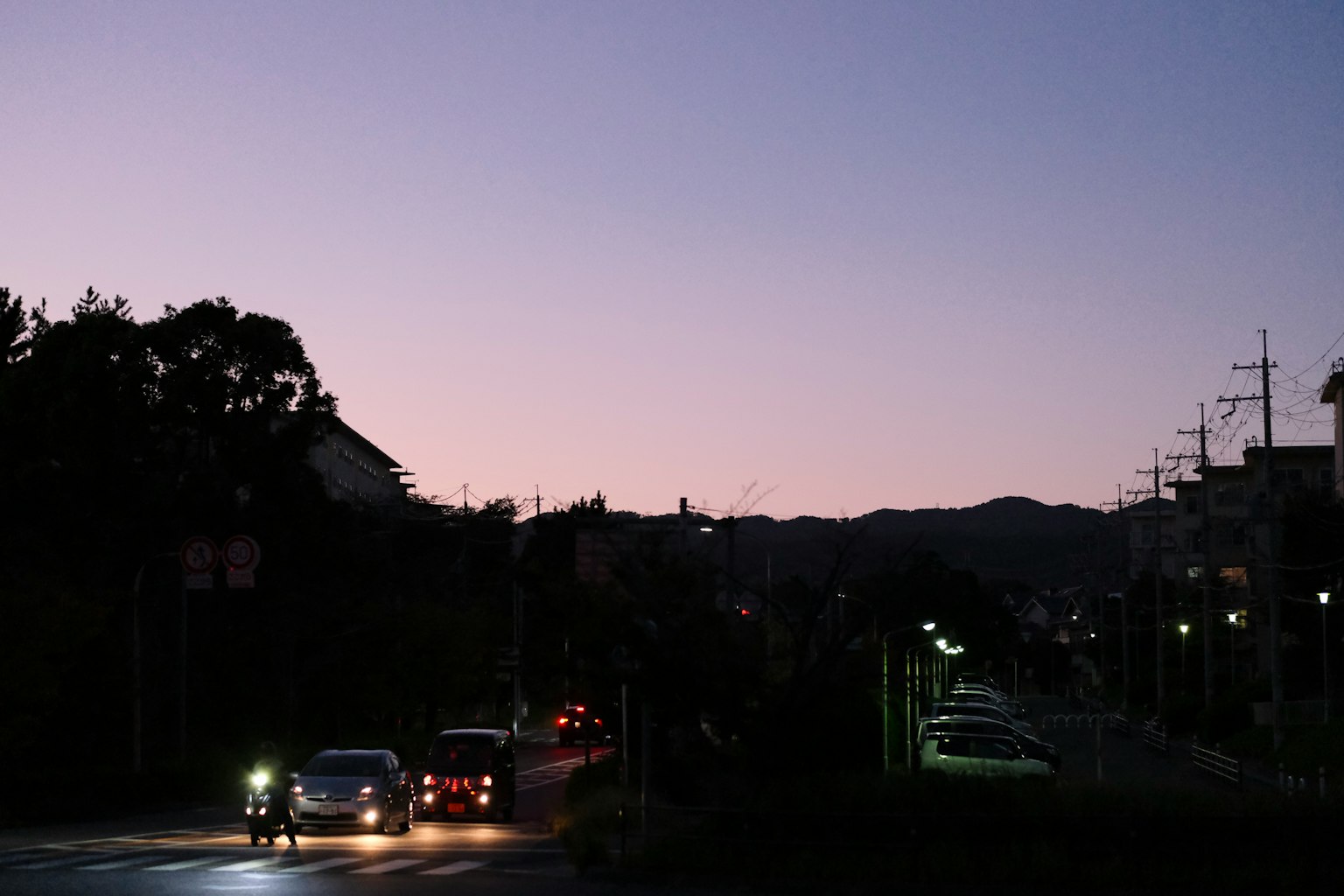 Cars on a street at dusk with silhouettes of hills