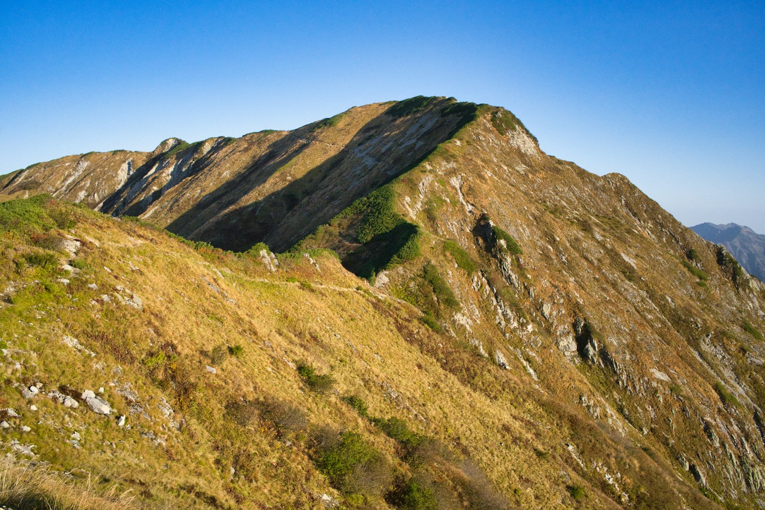 Sommet de montagne avec des pentes herbeuses et un terrain rocheux sous un ciel bleu clair
