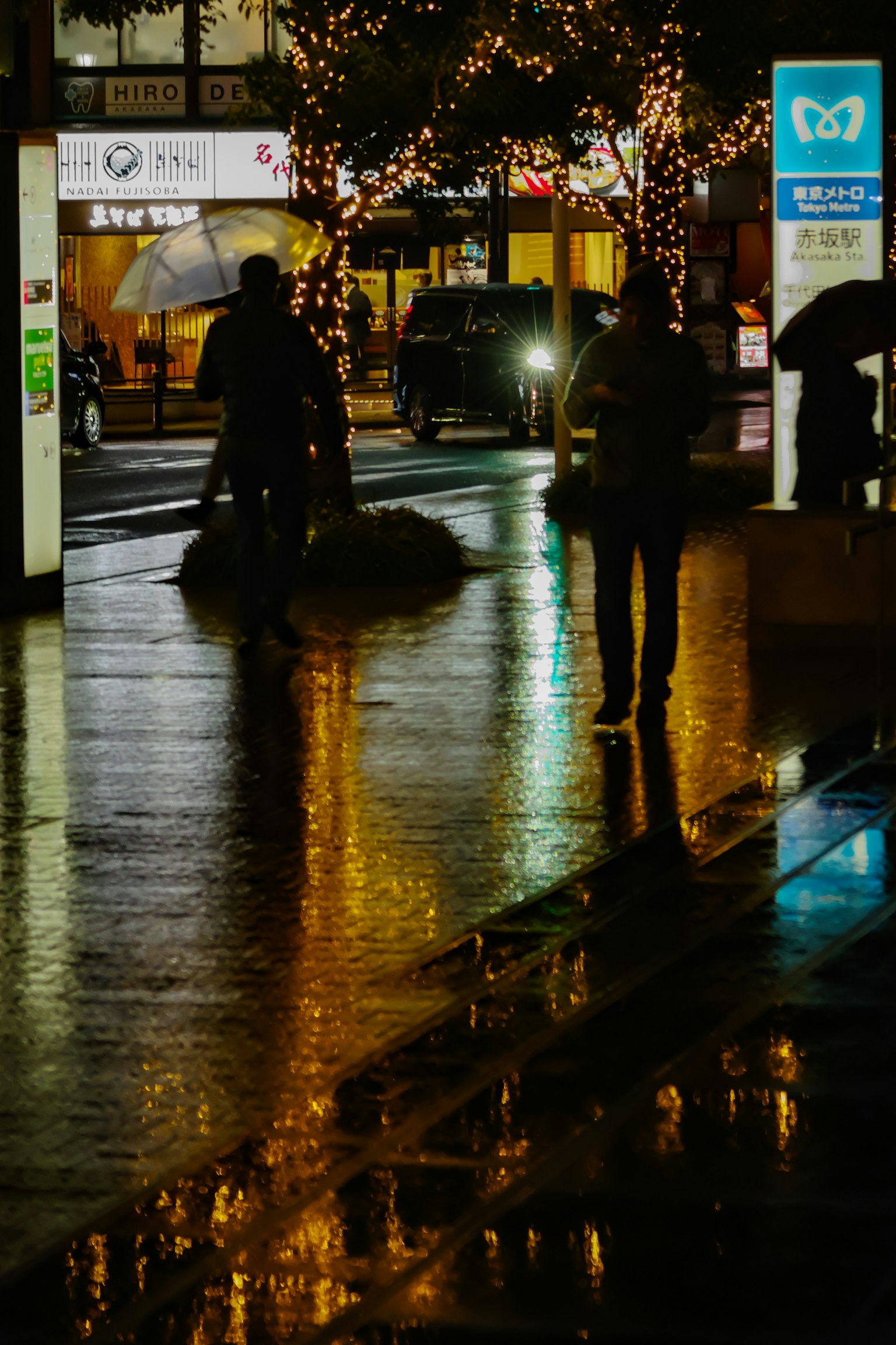 夜間城市景觀中,撐著傘的人們在濕滑人行道上的輪廓