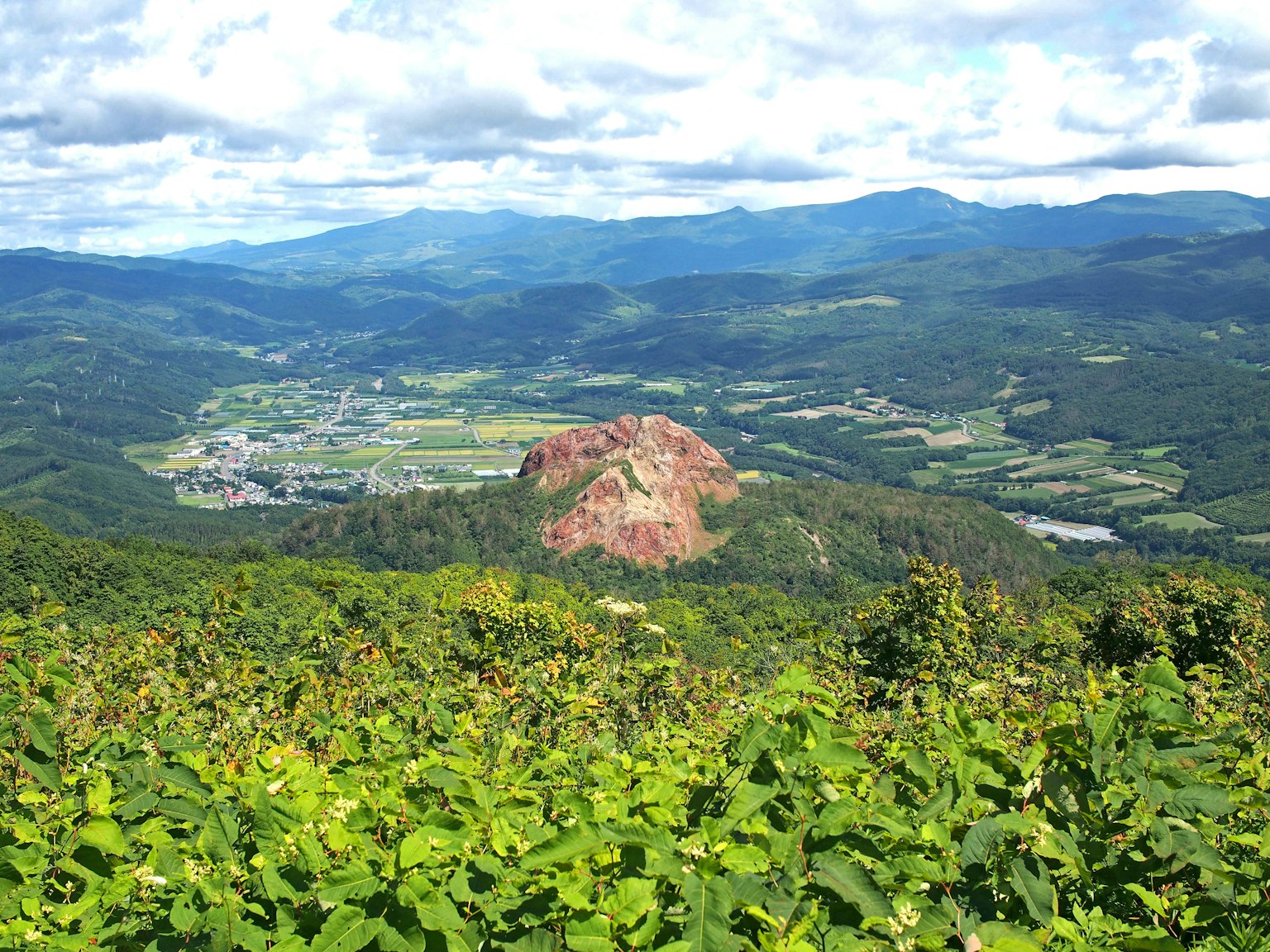 ทิวทัศน์ภูเขาที่สวยงามล้อมรอบด้วยพืชเขียวขจีและก้อนหินสีแดงที่โดดเด่น