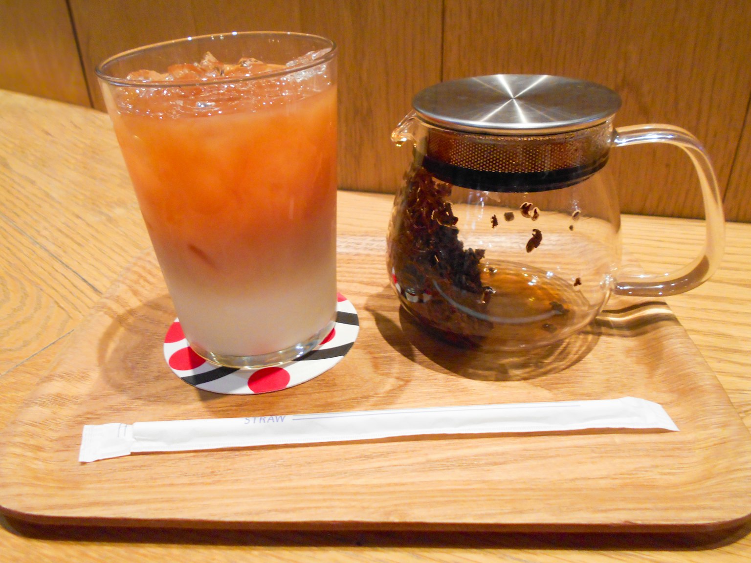 Glas mit Eistee in Schichten und eine Teekanne auf einem Holztablett