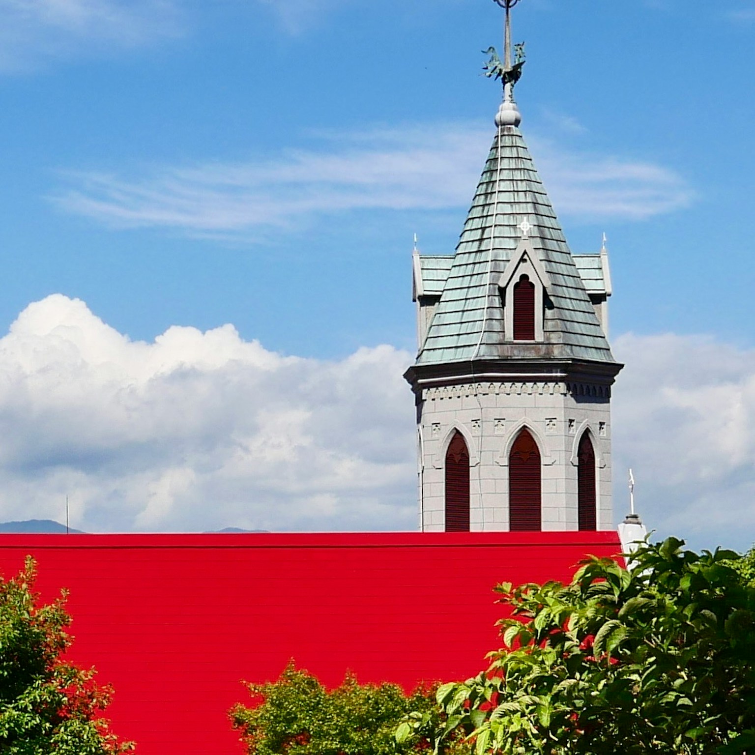 Menara gereja dengan atap runcing dan atap merah terlihat di bawah langit biru