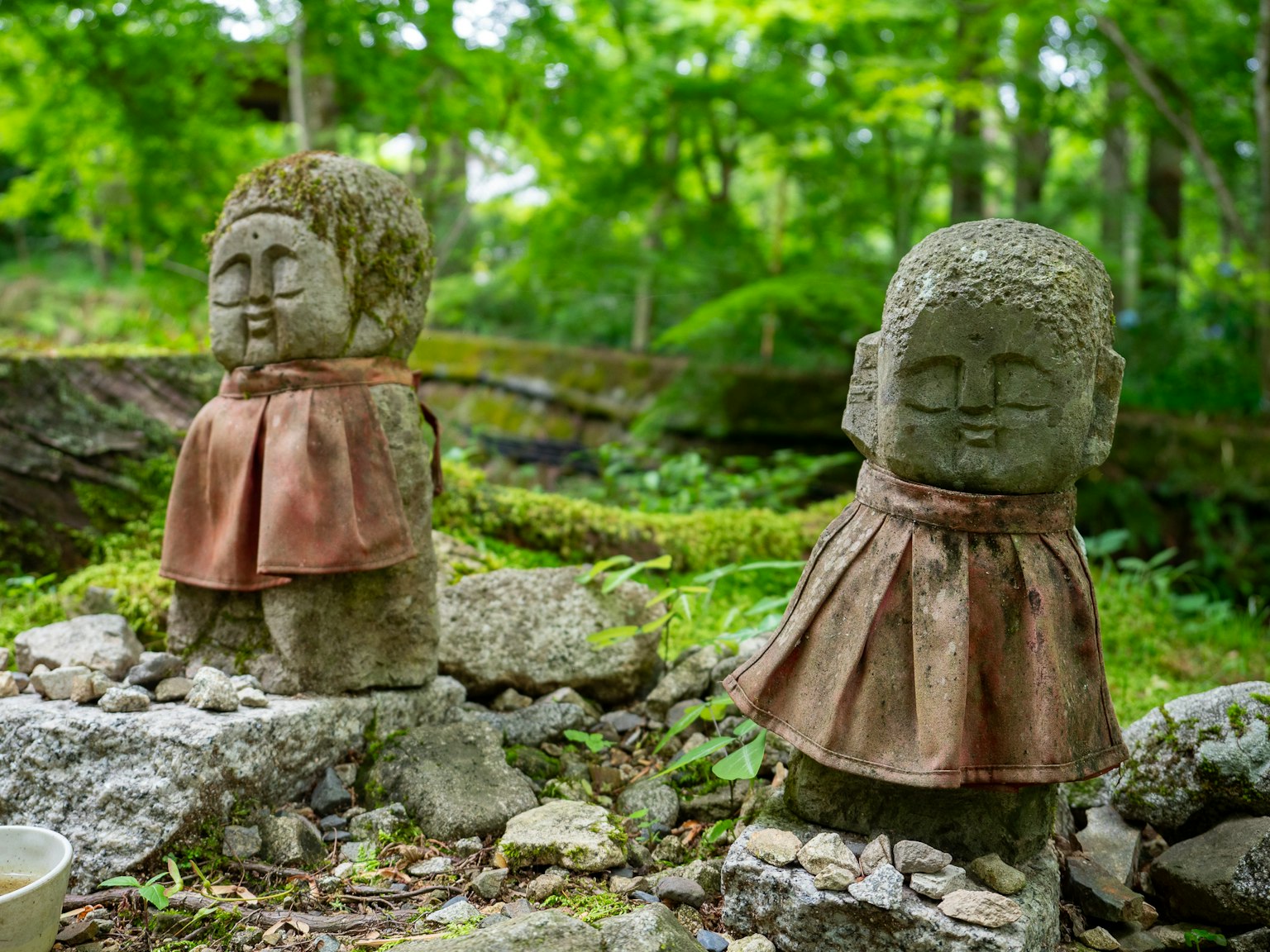 Dos estatuas de piedra en un bosque verde que llevan tela roja