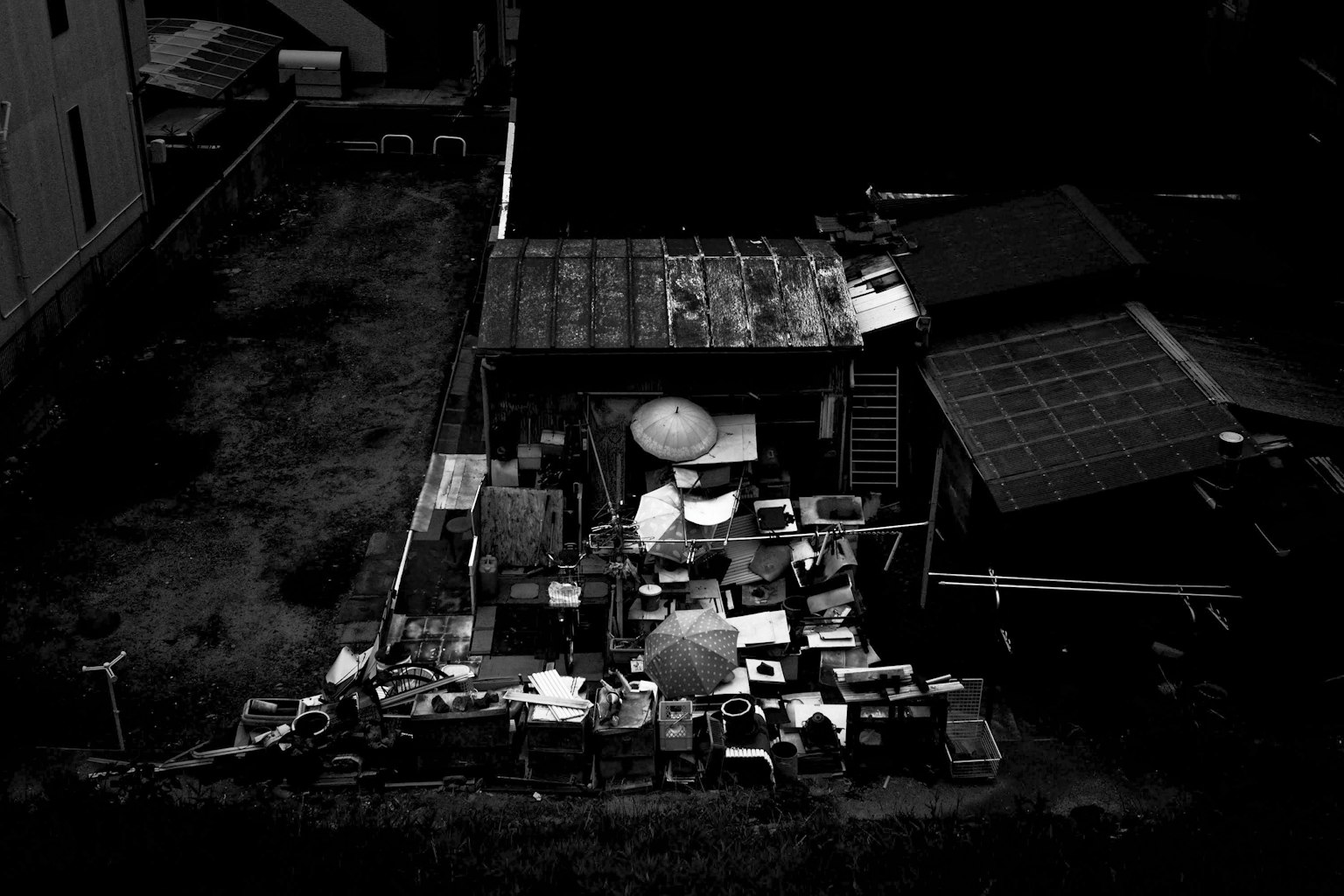 Photo en noir et blanc d'un espace extérieur avec des objets éparpillés et un bâtiment couvert