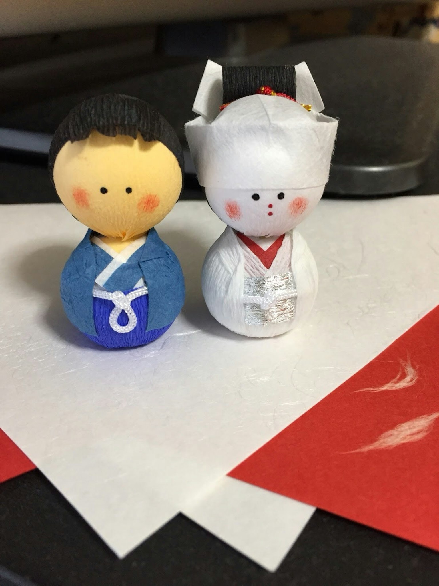 Deux petites poupées japonaises côte à côte le garçon porte un costume bleu et la fille porte un costume blanc