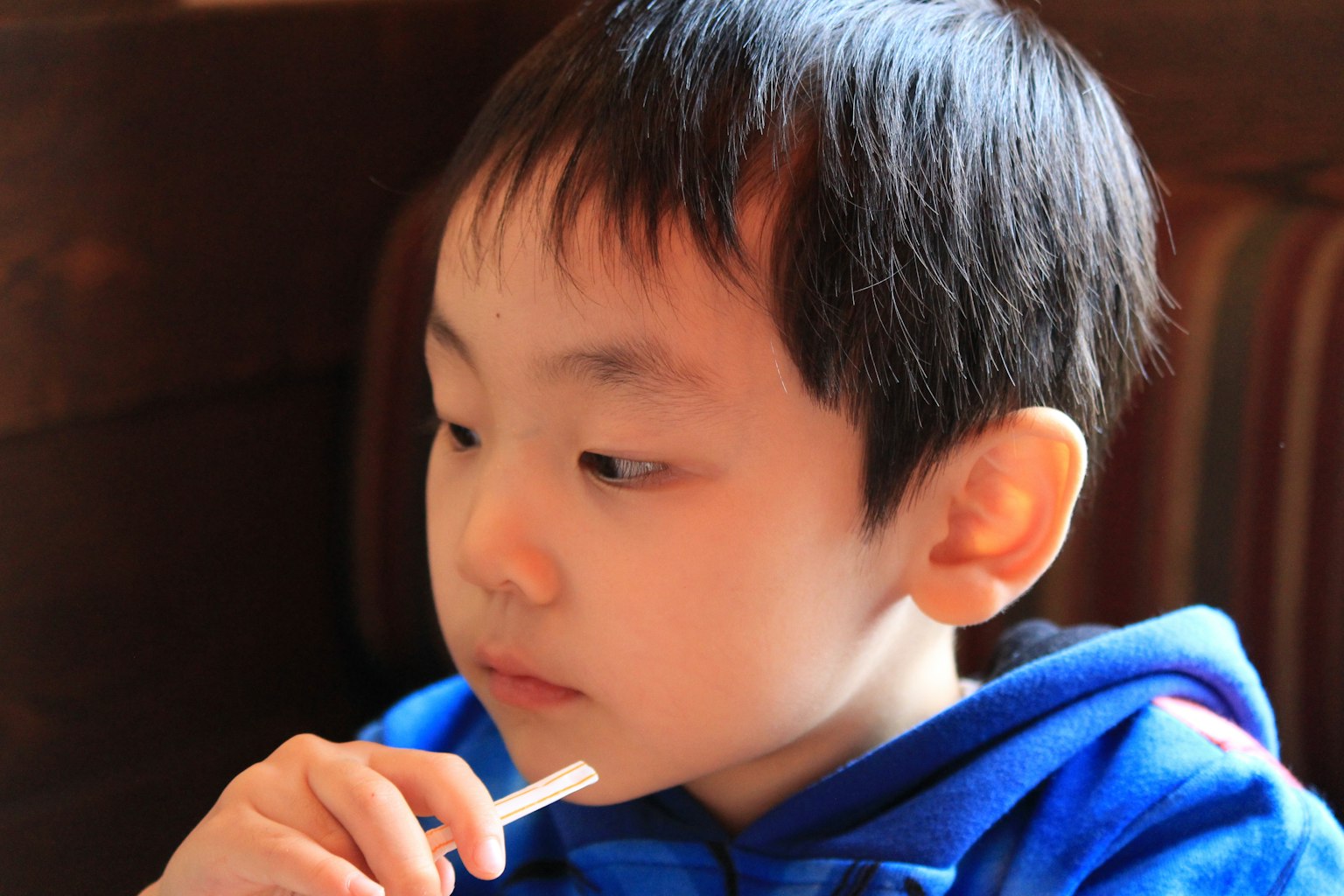 Seorang anak laki-laki mengenakan hoodie biru memegang sedotan dengan berpikir