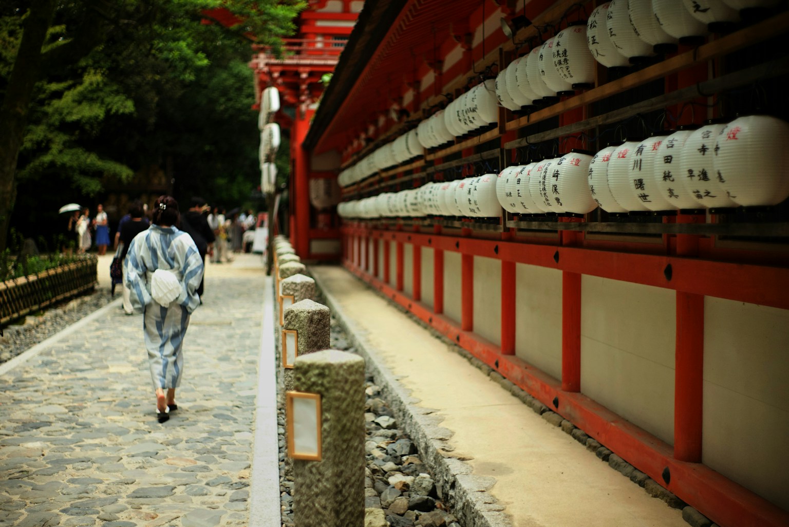 伝統的な浴衣を着た人が散策する神社の小道と赤い建物