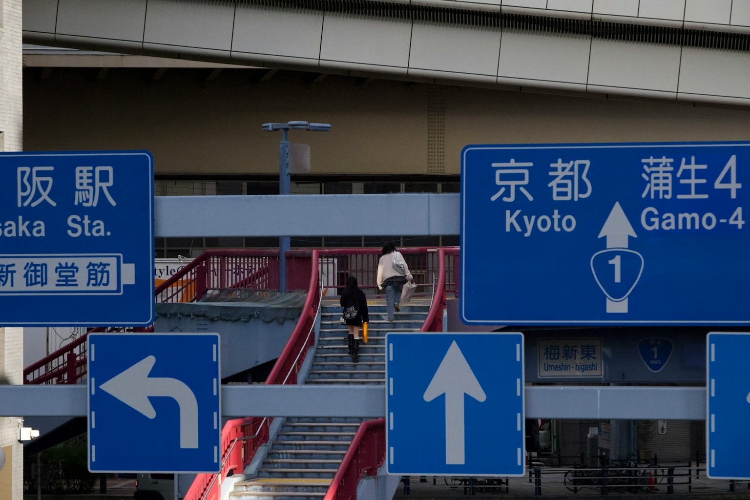 人们正在上楼梯，蓝色标志指示大阪站和京都目的地