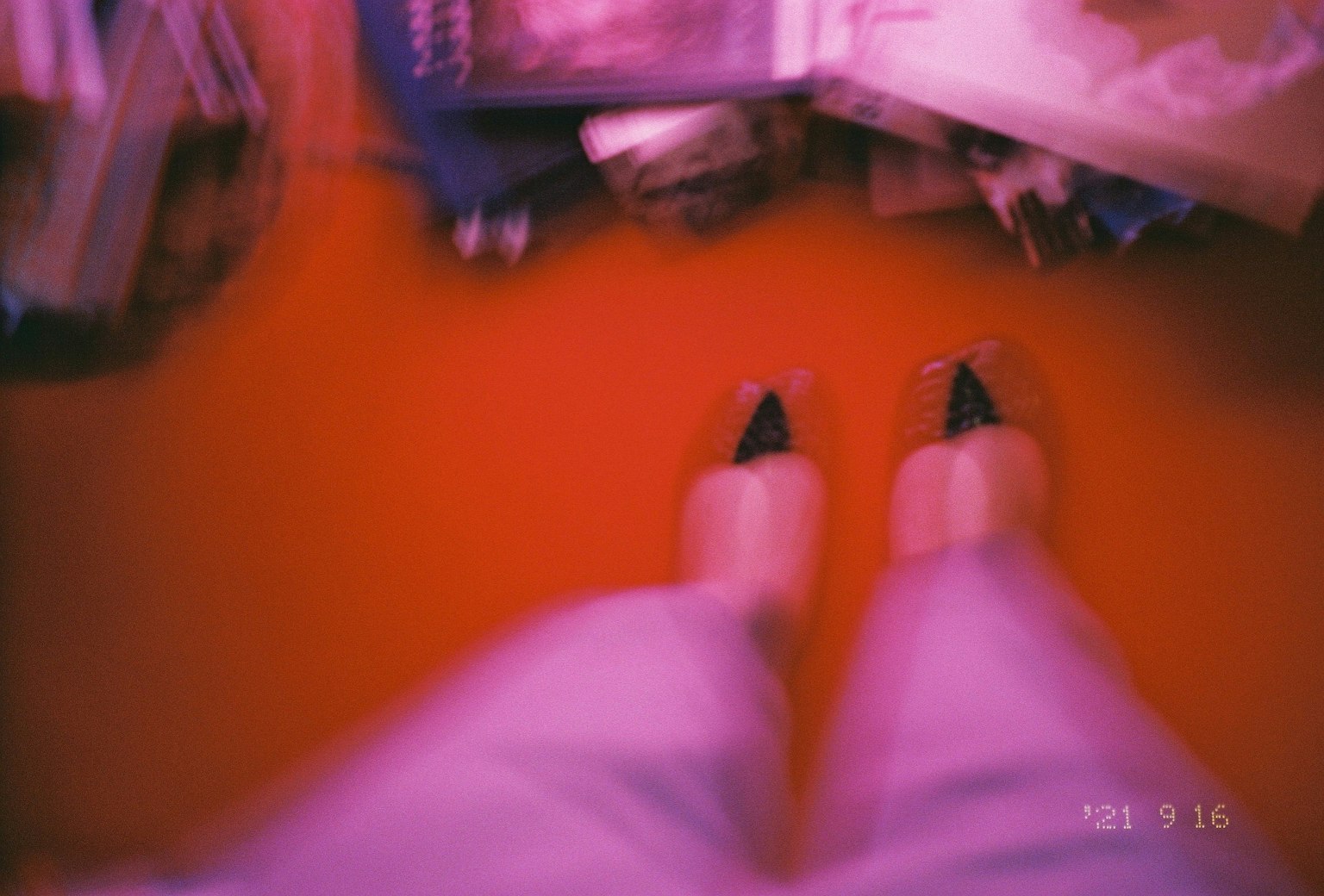 Blurred photo of feet standing on a red floor showing sandals and surrounding books