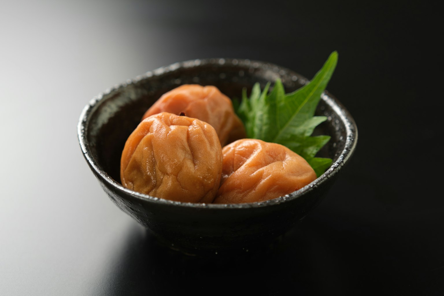 黑色碗中的梅子和绿色装饰