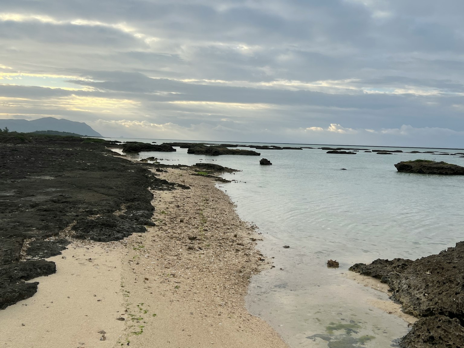 Pemandangan indah pantai berpasir dan garis pantai berbatu di bawah langit mendung dengan air tenang