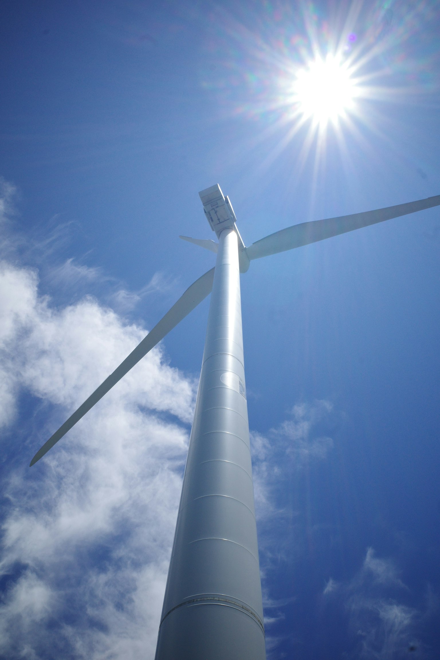 風力発電機の下からの視点で青空と太陽が見える