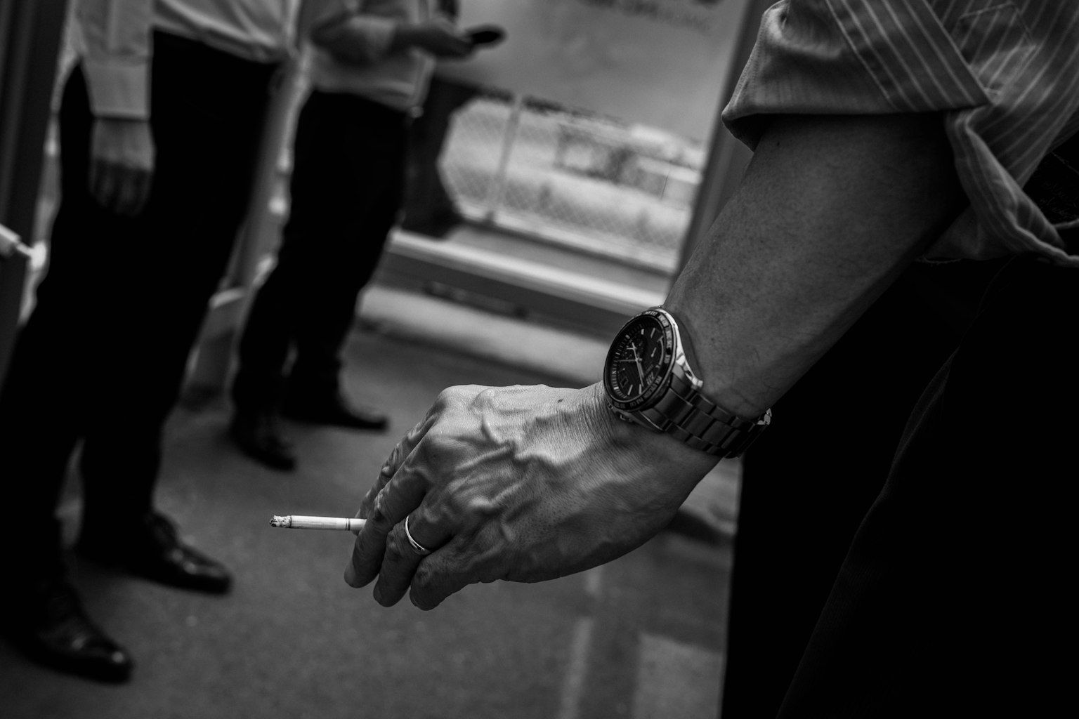ภาพขาวดำของมือผู้ชายที่ถือบุหรี่พร้อมนาฬิกาที่ข้อมือ