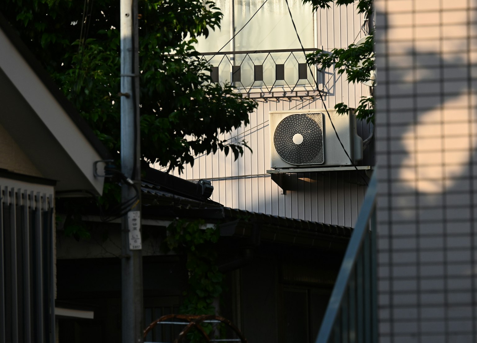 Façade d'un bâtiment avec une unité de climatisation et des ombres dans la rue