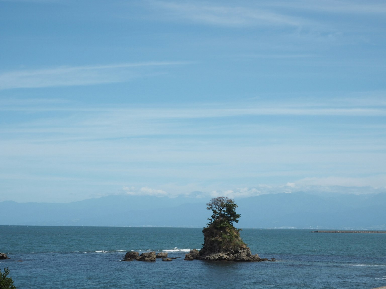 Una pequeña isla con árboles rodeada de mar azul y montañas distantes