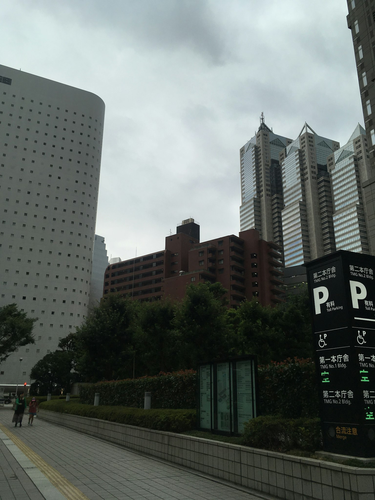 ทิวทัศน์เมืองที่มีอาคารและพืชพรรณใต้ท้องฟ้าที่มีเมฆพร้อมป้ายจอดรถ