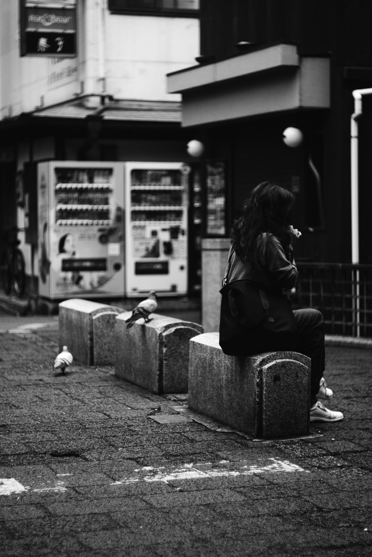 Femme assise sur un banc dans une scène de rue en noir et blanc avec des pigeons