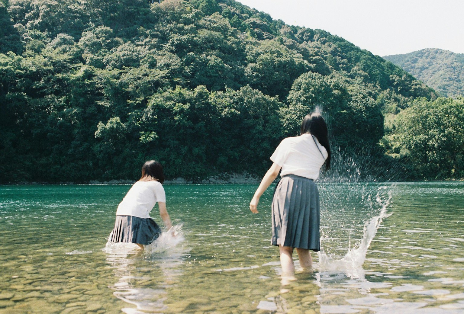 Deux filles jouant dans l'eau peu profonde avec des collines vertes en arrière-plan