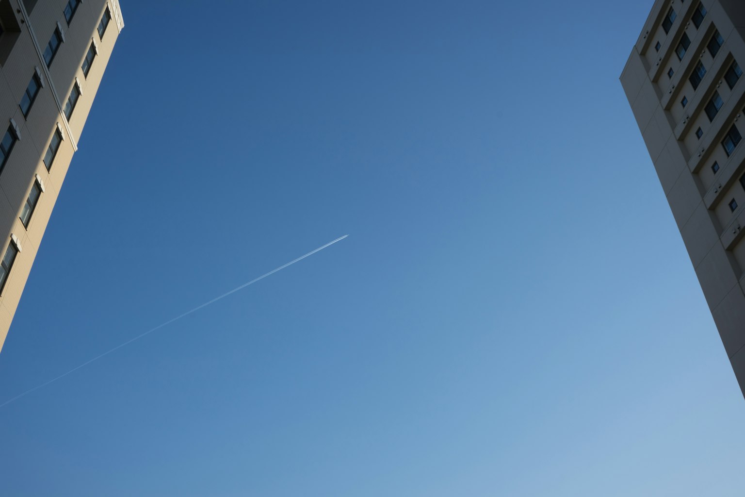 Vue entre des bâtiments avec un traînée d'avion dans le ciel bleu